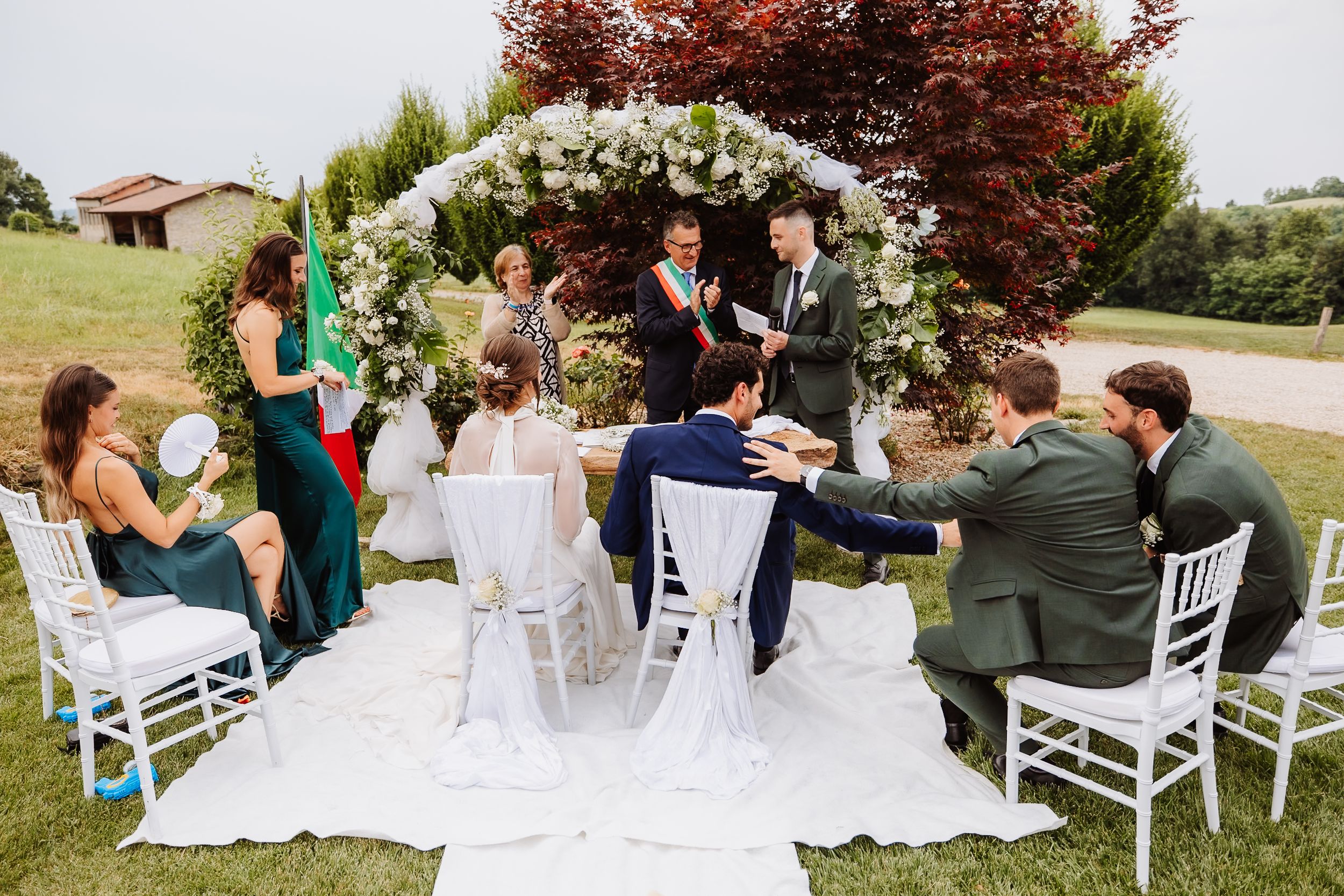 Guests mingle and celebrate at an outdoor wedding reception with white chairs arranged on a grassy lawn.