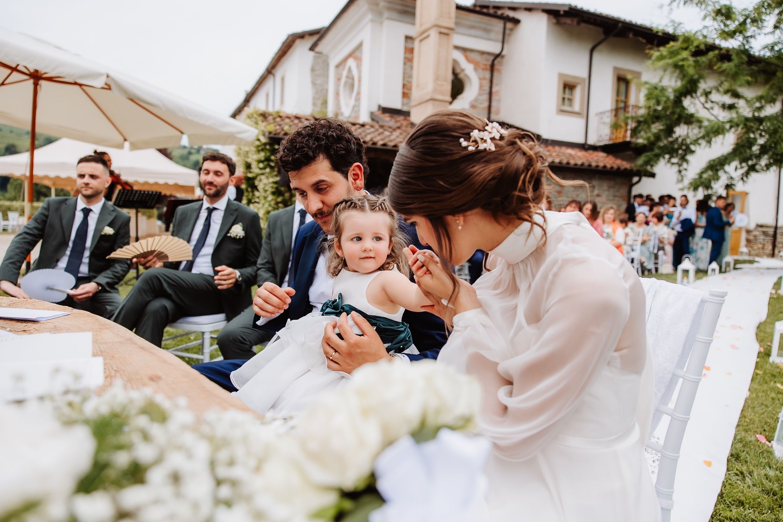 People gather at an outdoor wedding reception with white floral centerpieces and table settings at a rustic venue.