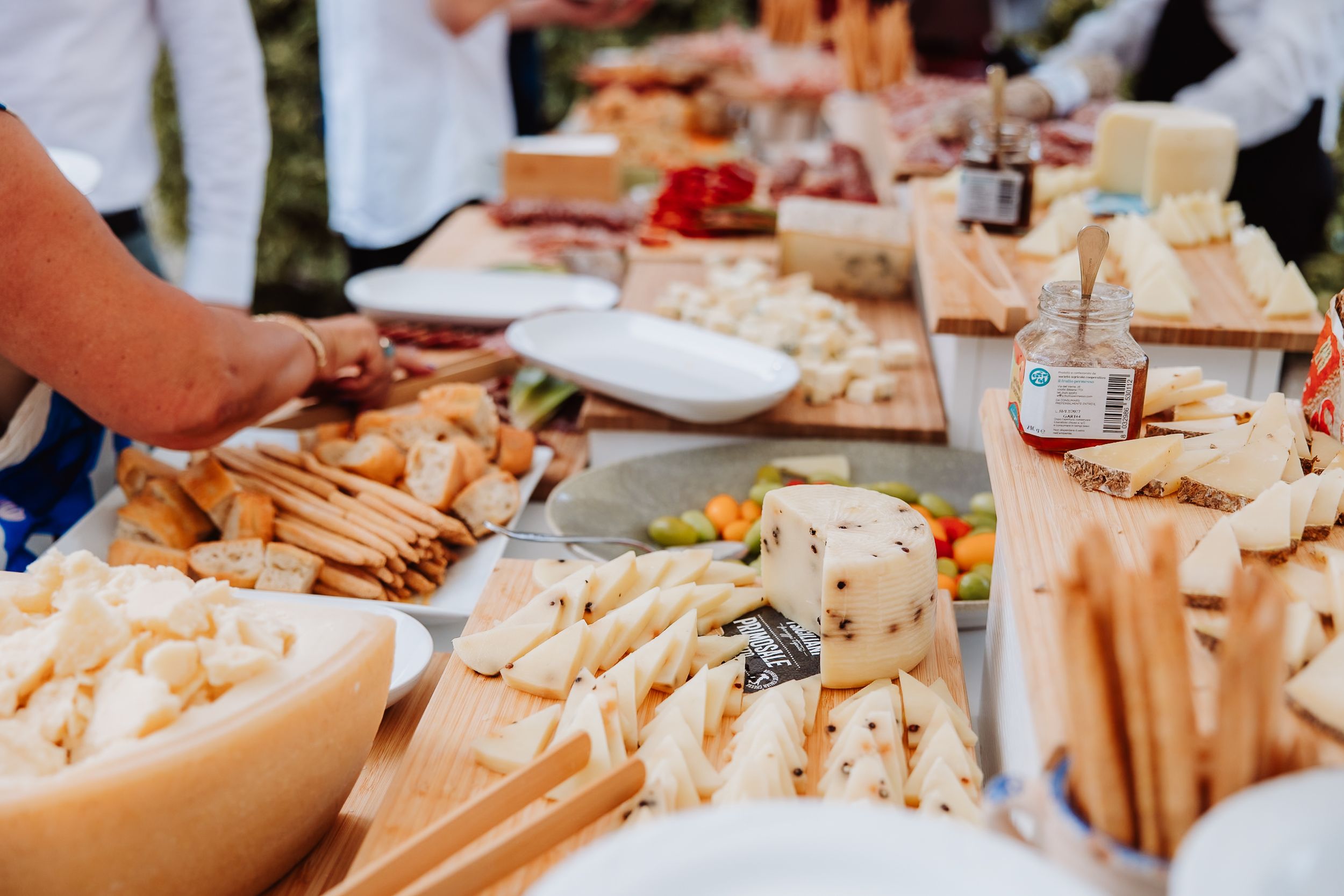 Fresh charcuterie board spread with assorted meats, cheeses and breadsticks laid out on white tablecloth at outdoor event.