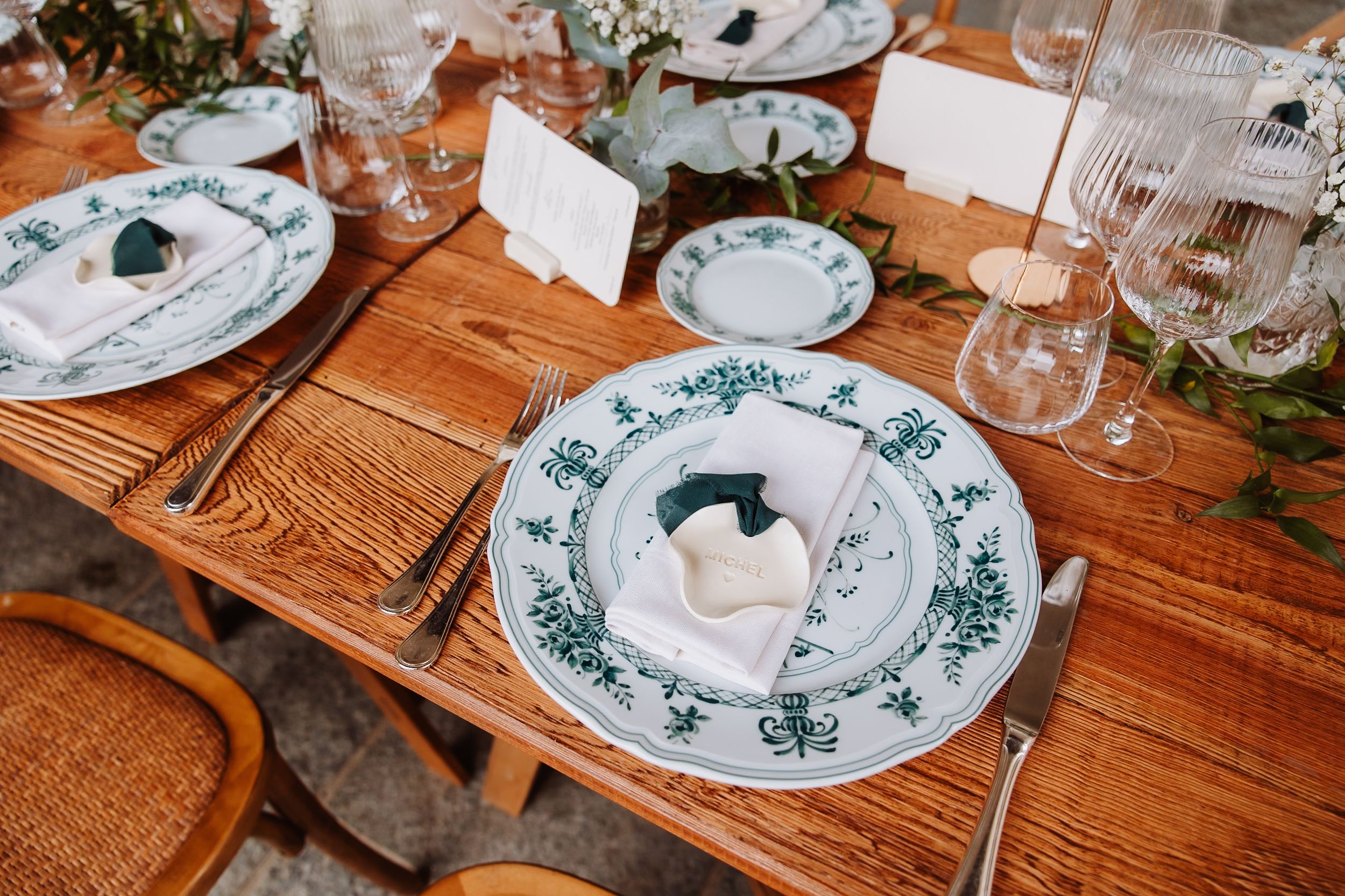 Rustic wooden table set with elegant place settings featuring blue floral patterned plates and name cards.