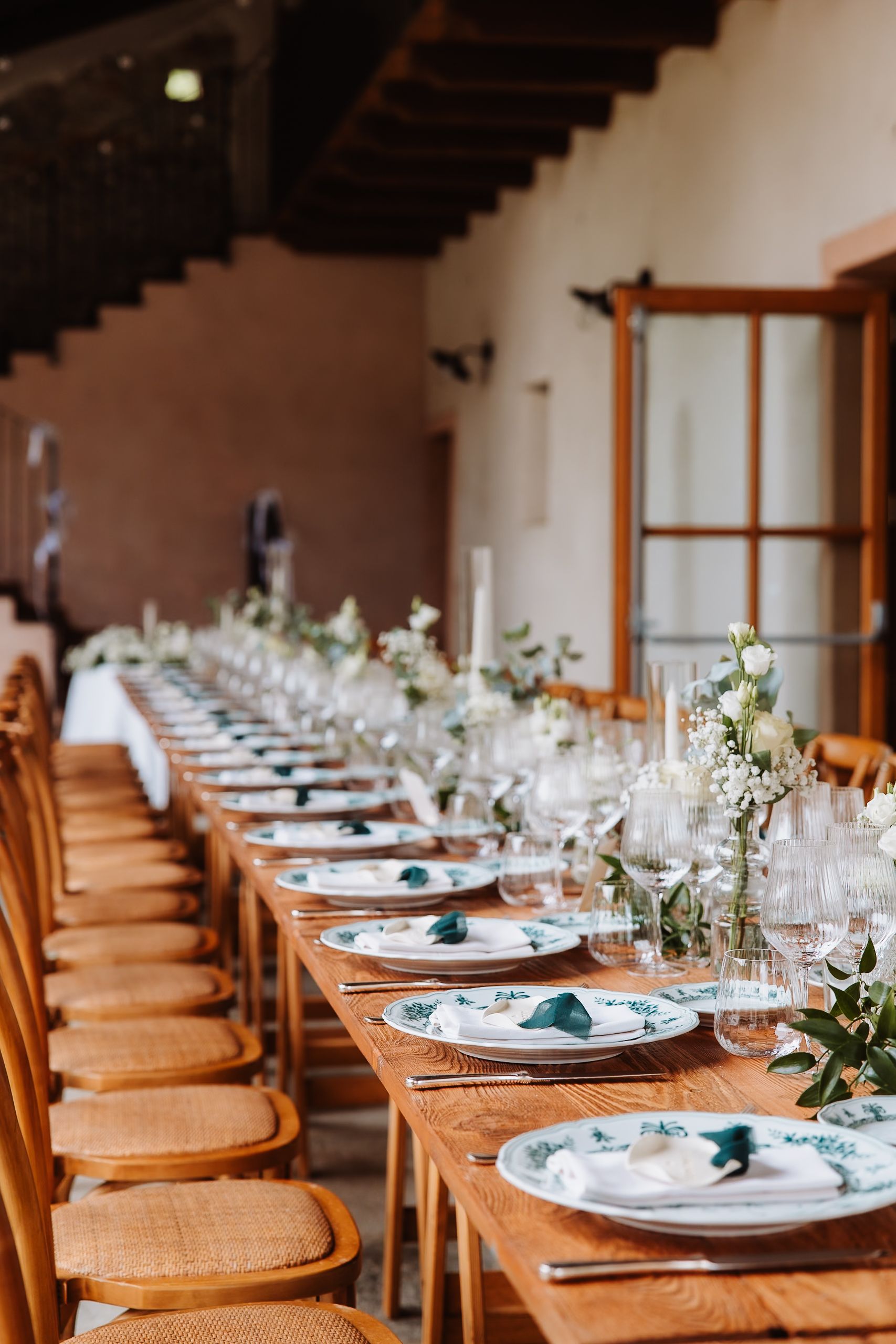 Elegant wedding reception table setup with wooden chairs and white floral centerpieces at a rustic venue.