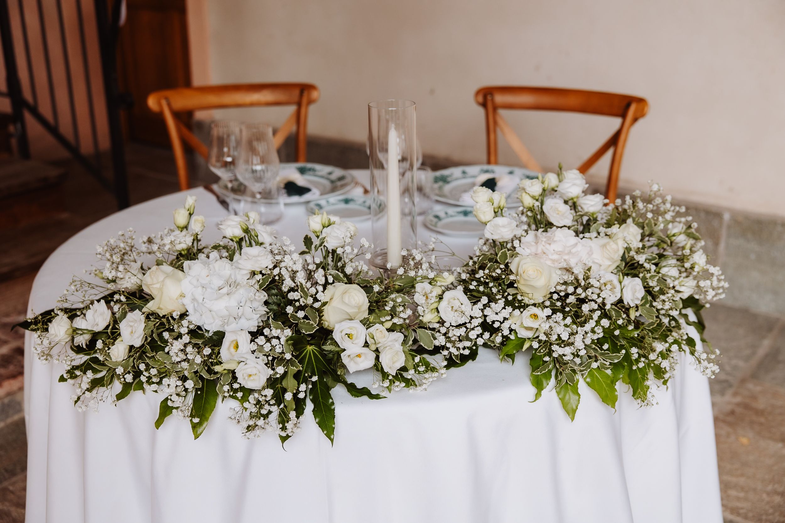 Elegant floral arrangement with white roses and baby's breath decorates a round table set with wine glasses.
