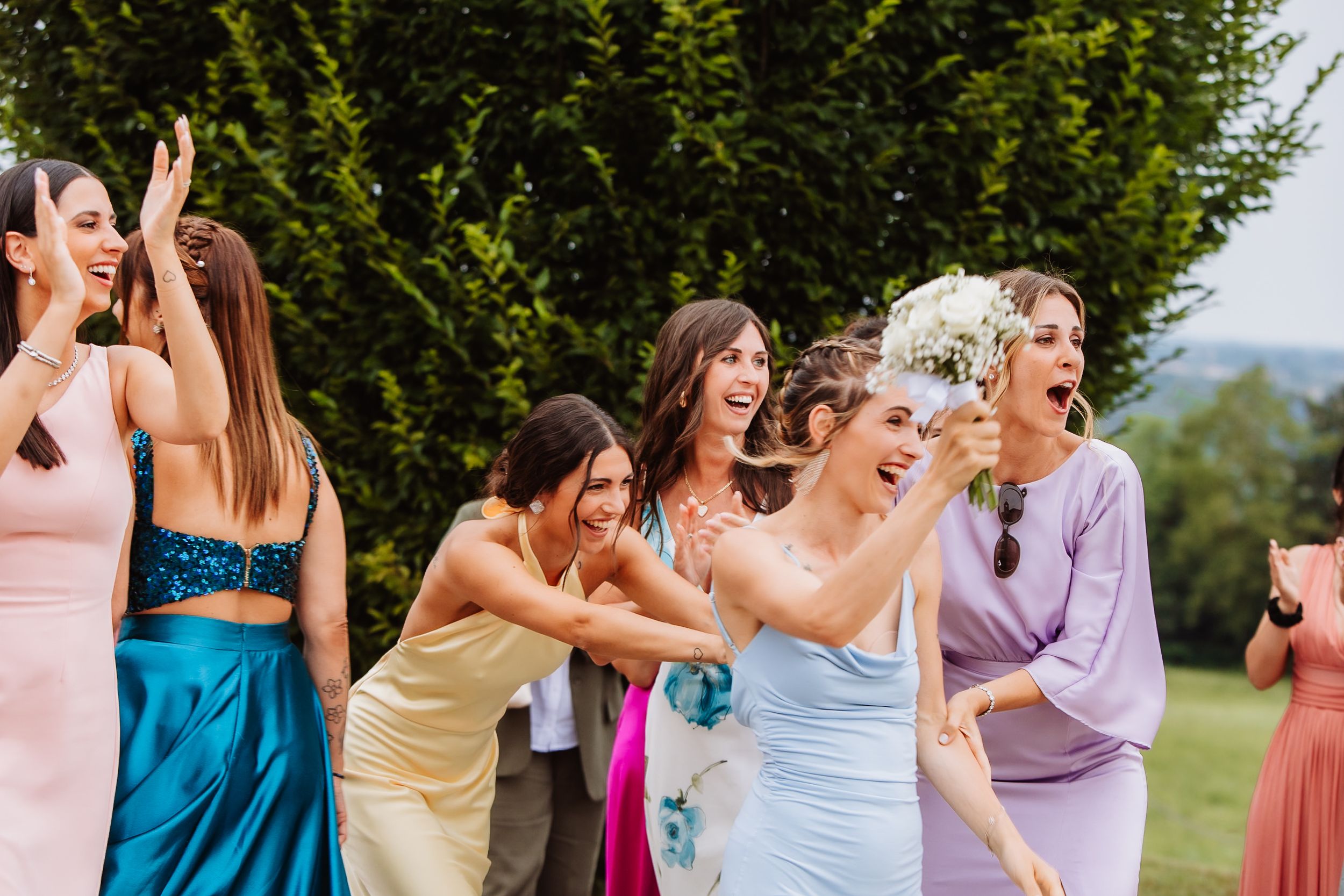 Group of bridesmaids in colorful dresses dancing together joyfully during outdoor wedding celebration.