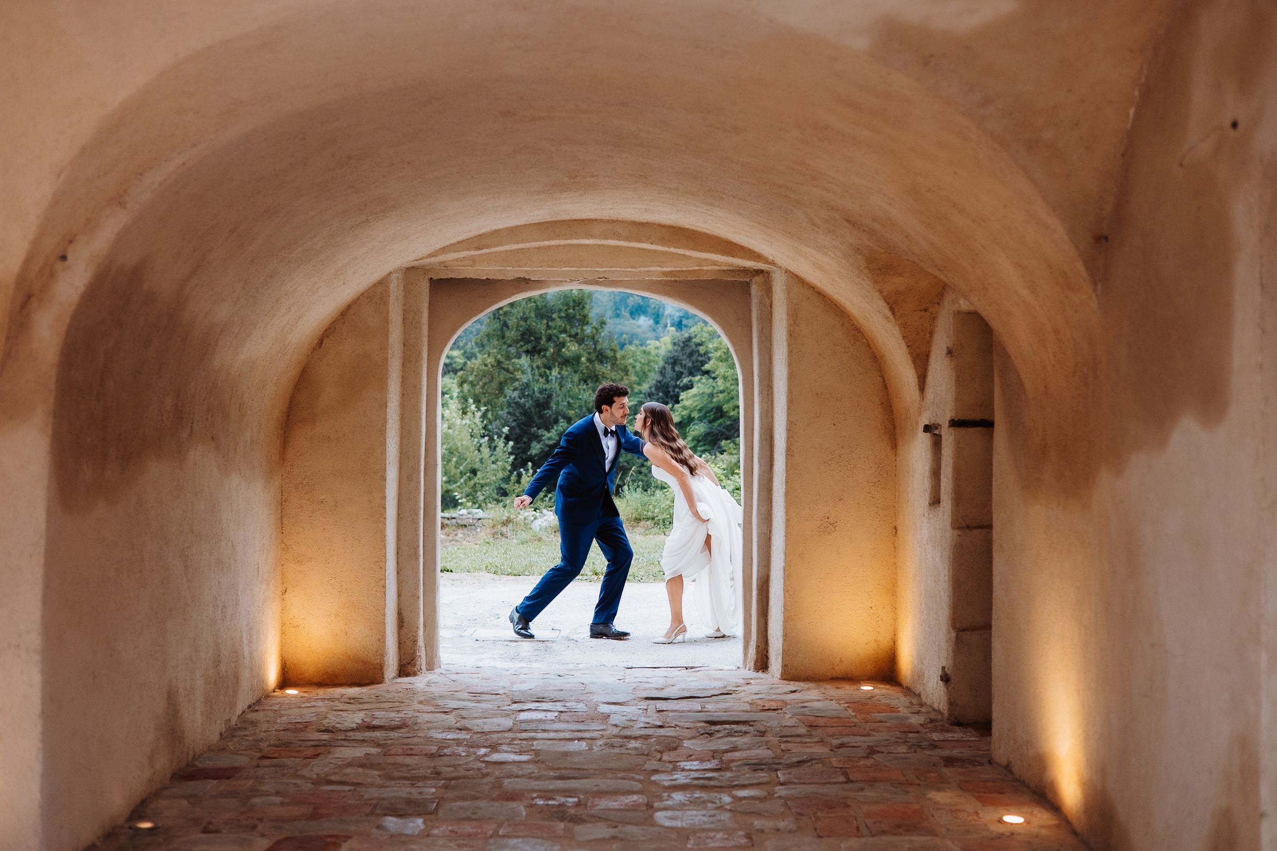 People in motion captured through a series of arched stone passageways with warm lighting along the corridor.