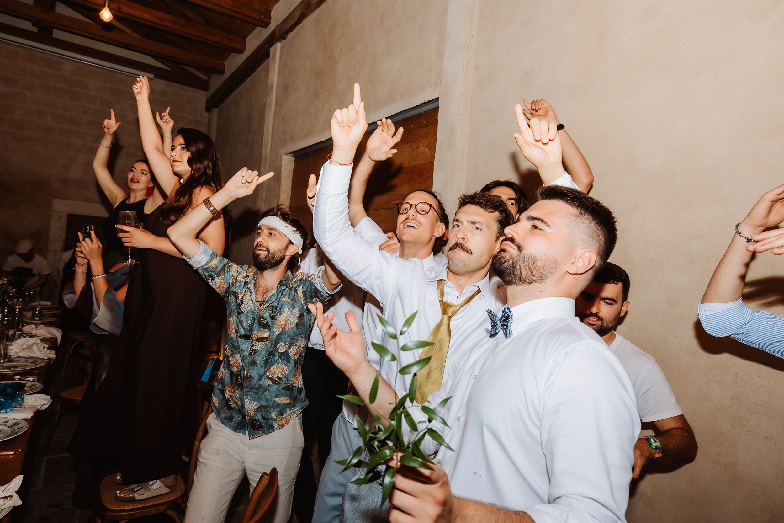 A group of party guests dance with raised arms and energetic expressions during a celebration.