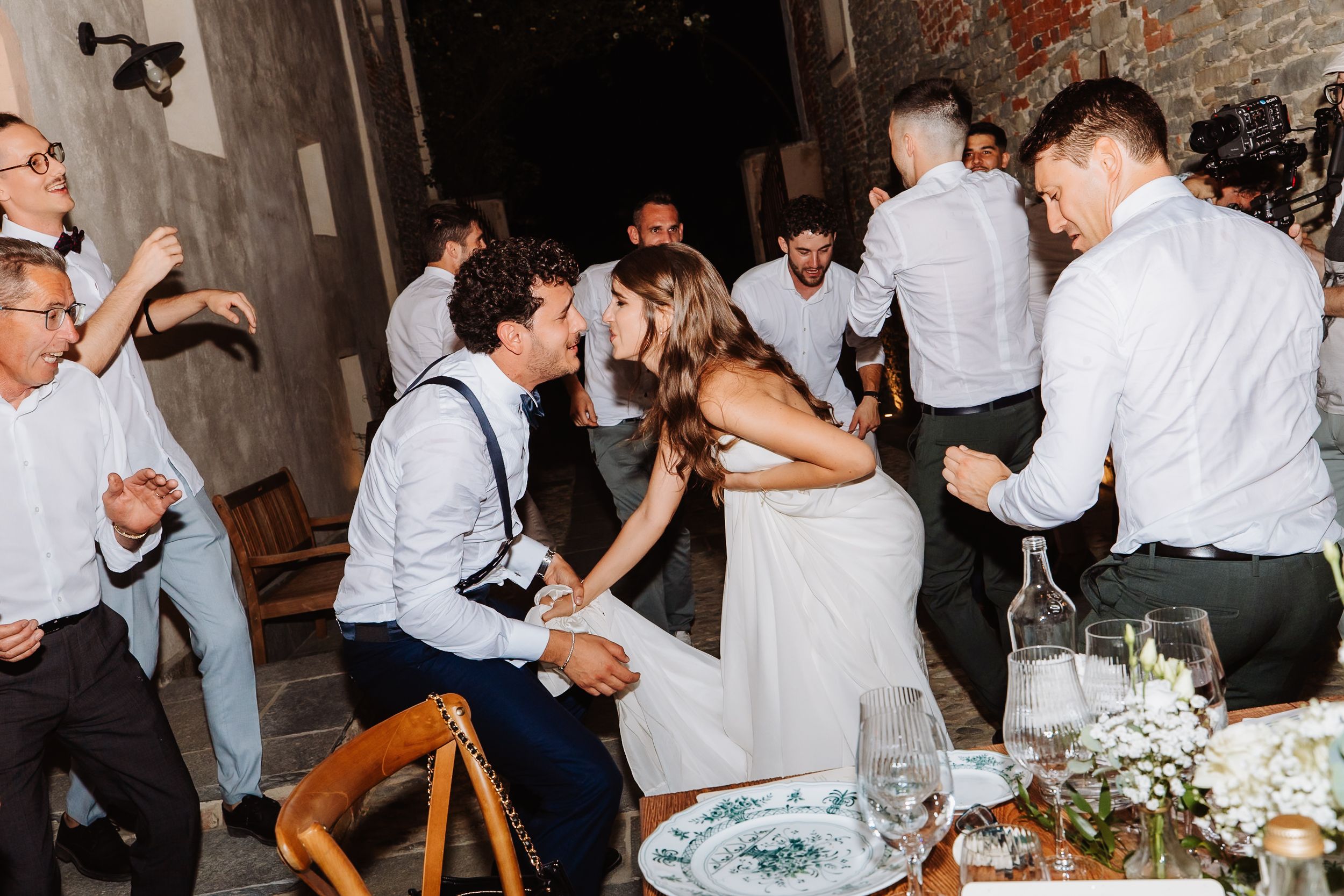 Wedding guests dance and celebrate at a reception dinner with rustic decor and white floral centerpieces.