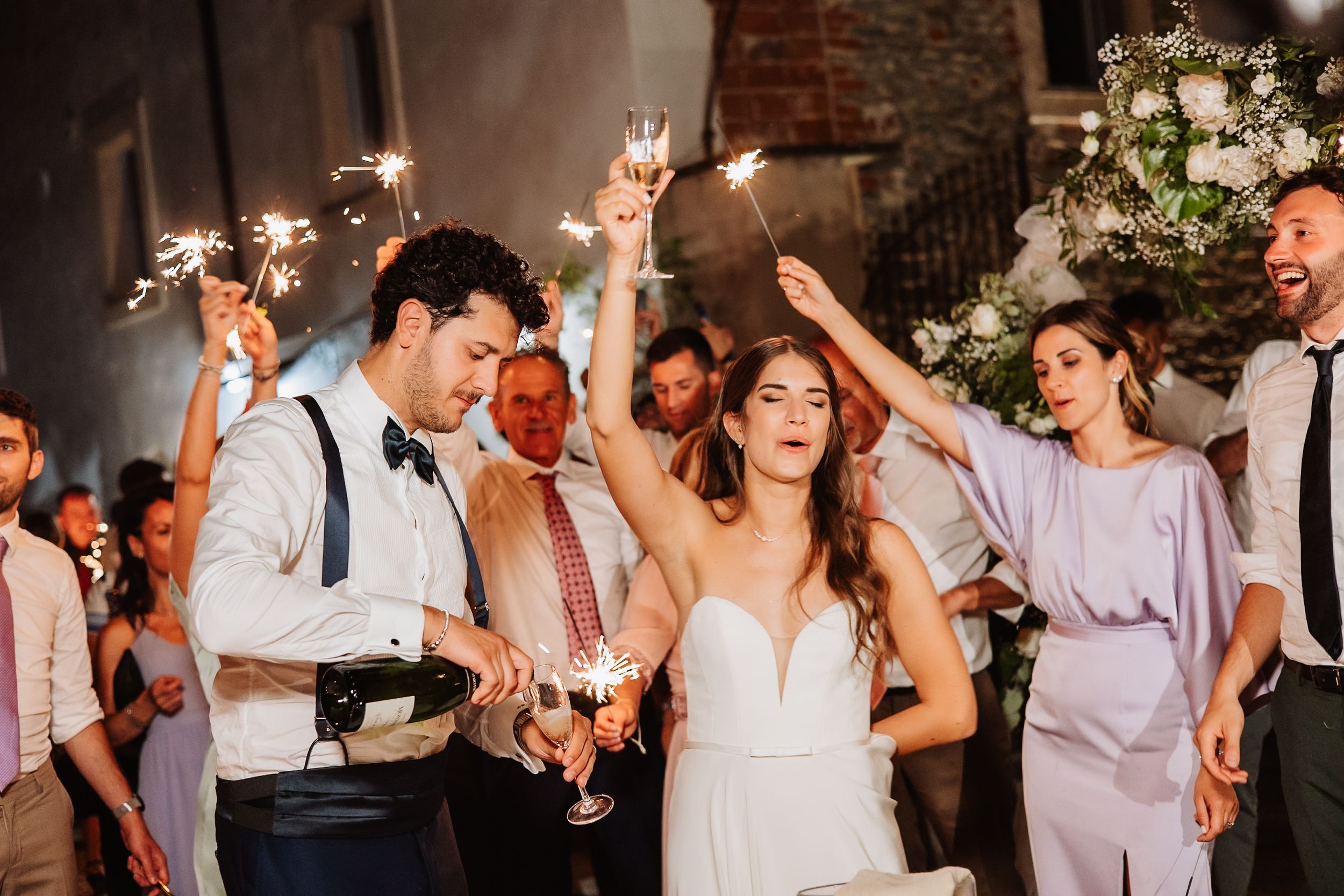 Wedding celebration with sparklers as guests dance and celebrate during evening reception party.