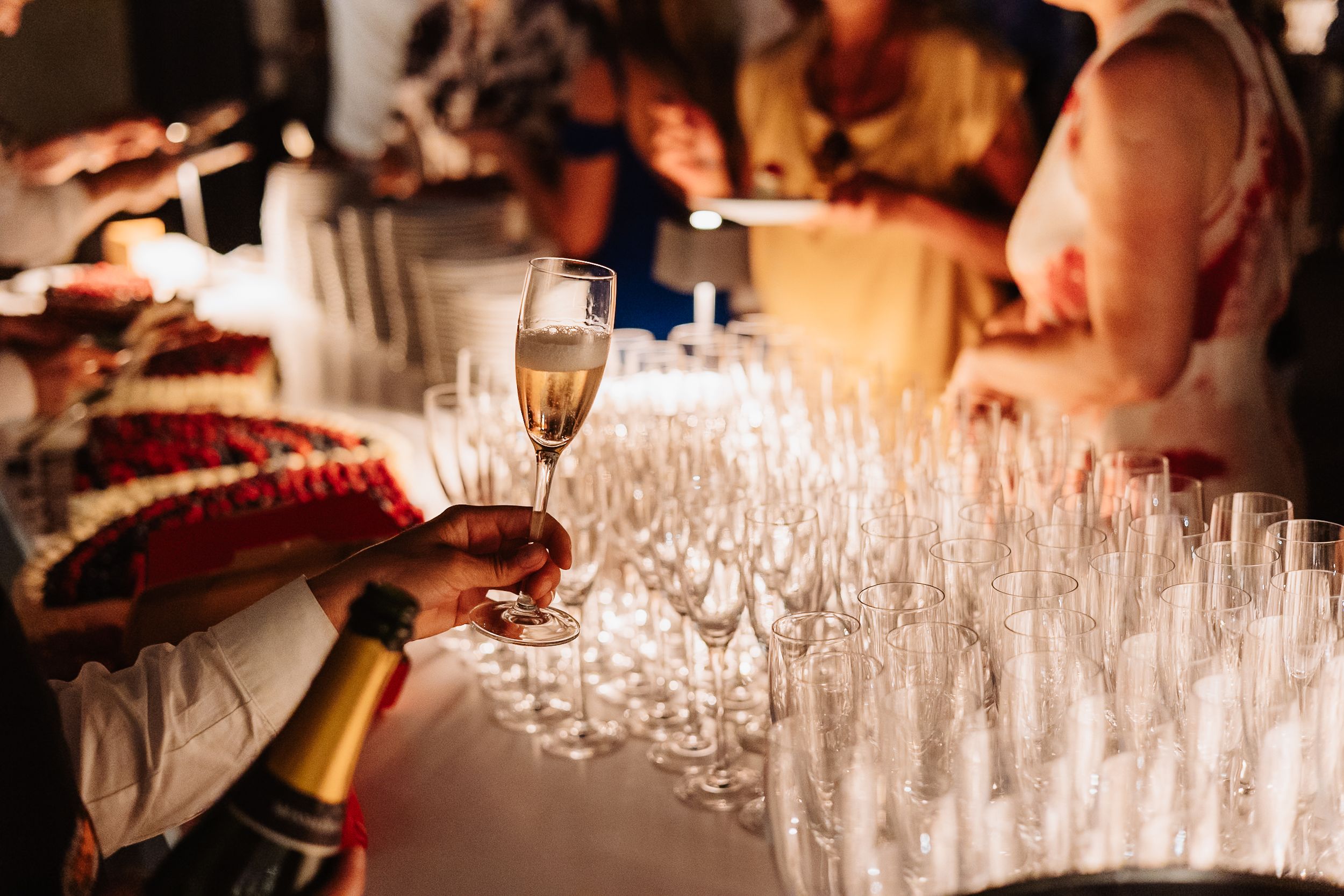 Long table filled with champagne flutes being served at an elegant event with warm ambient lighting.
