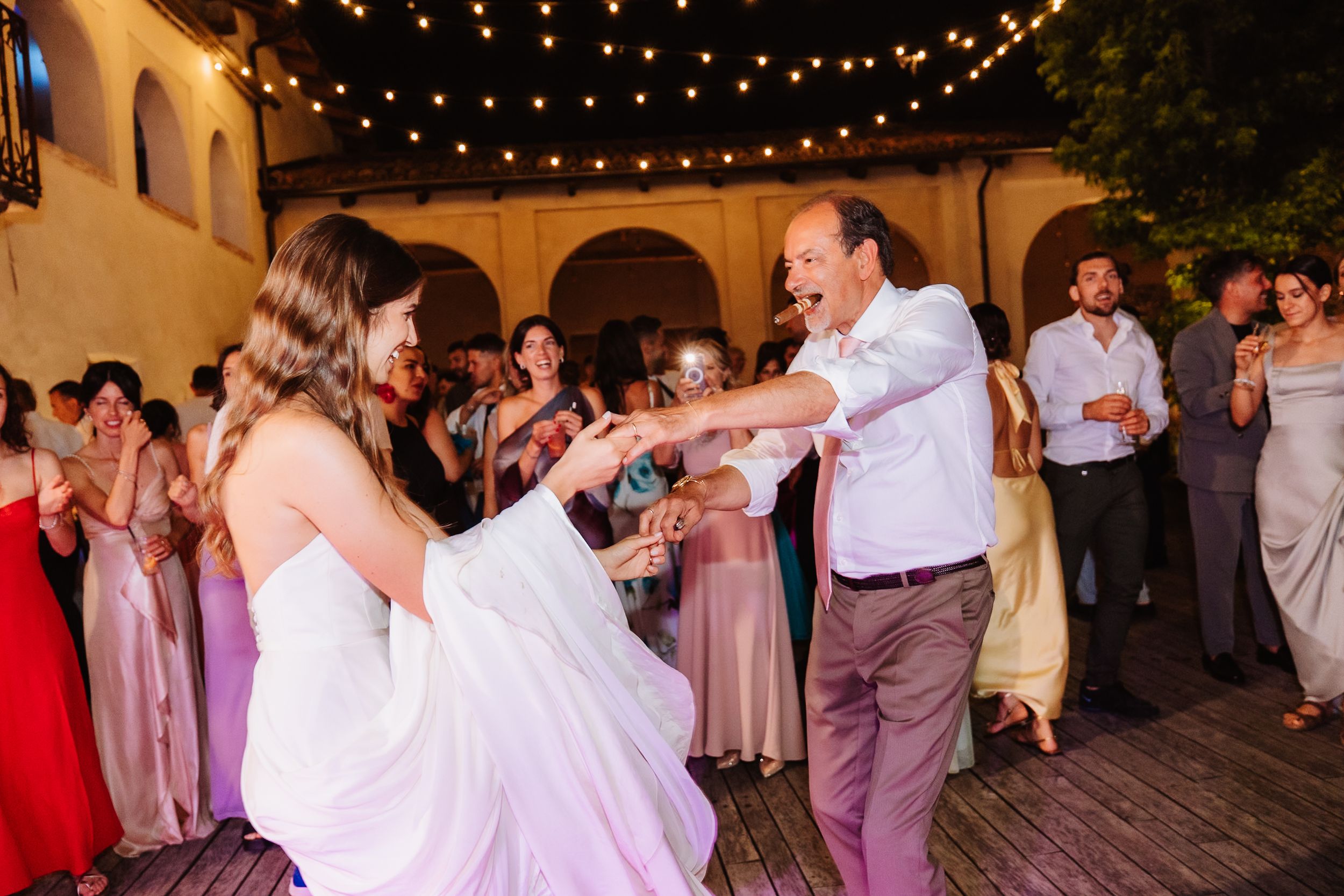 A couple dances together at an evening wedding reception under romantic string lights in a courtyard.