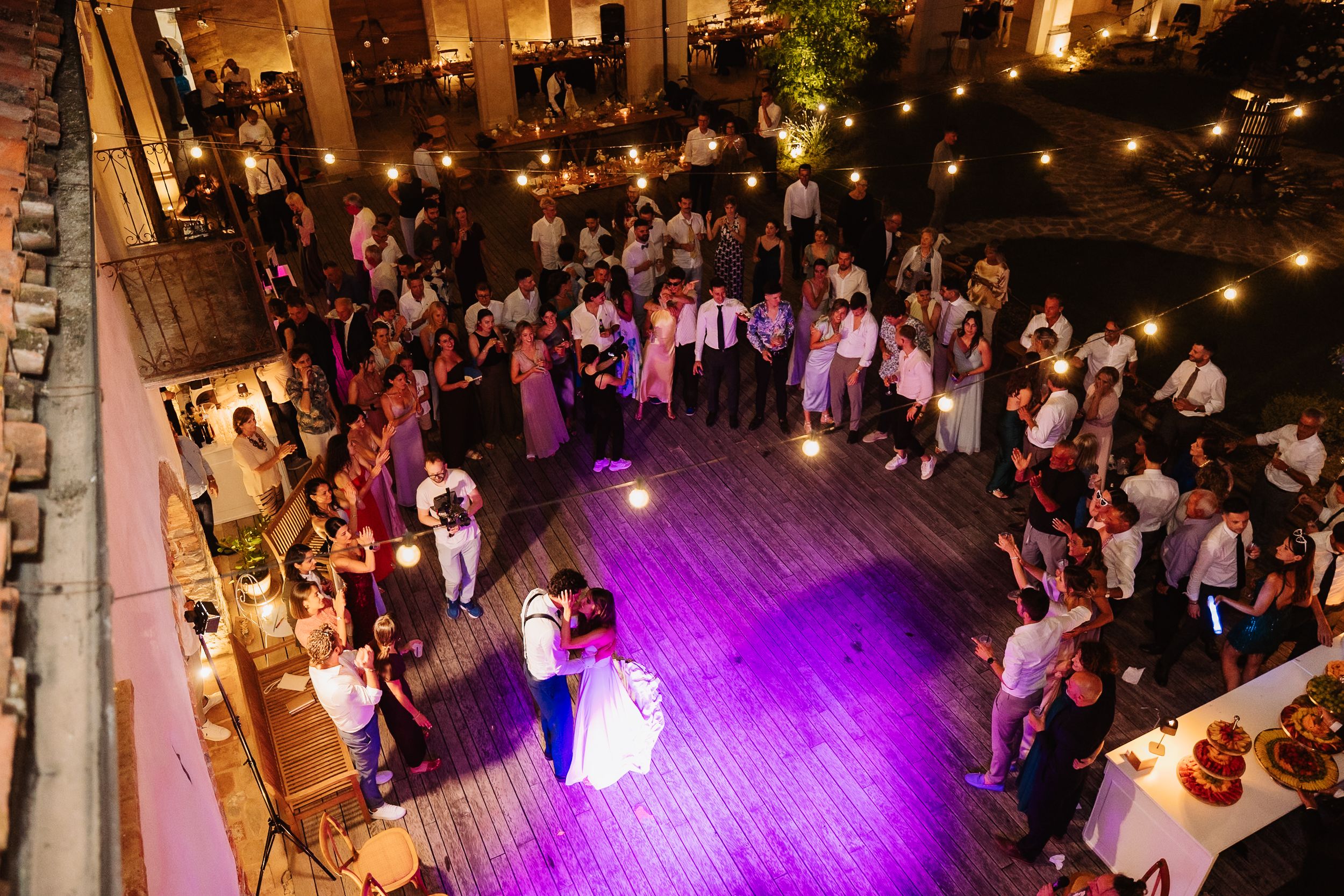 Wedding reception dance floor illuminated by purple lights with guests gathered around at an indoor venue.