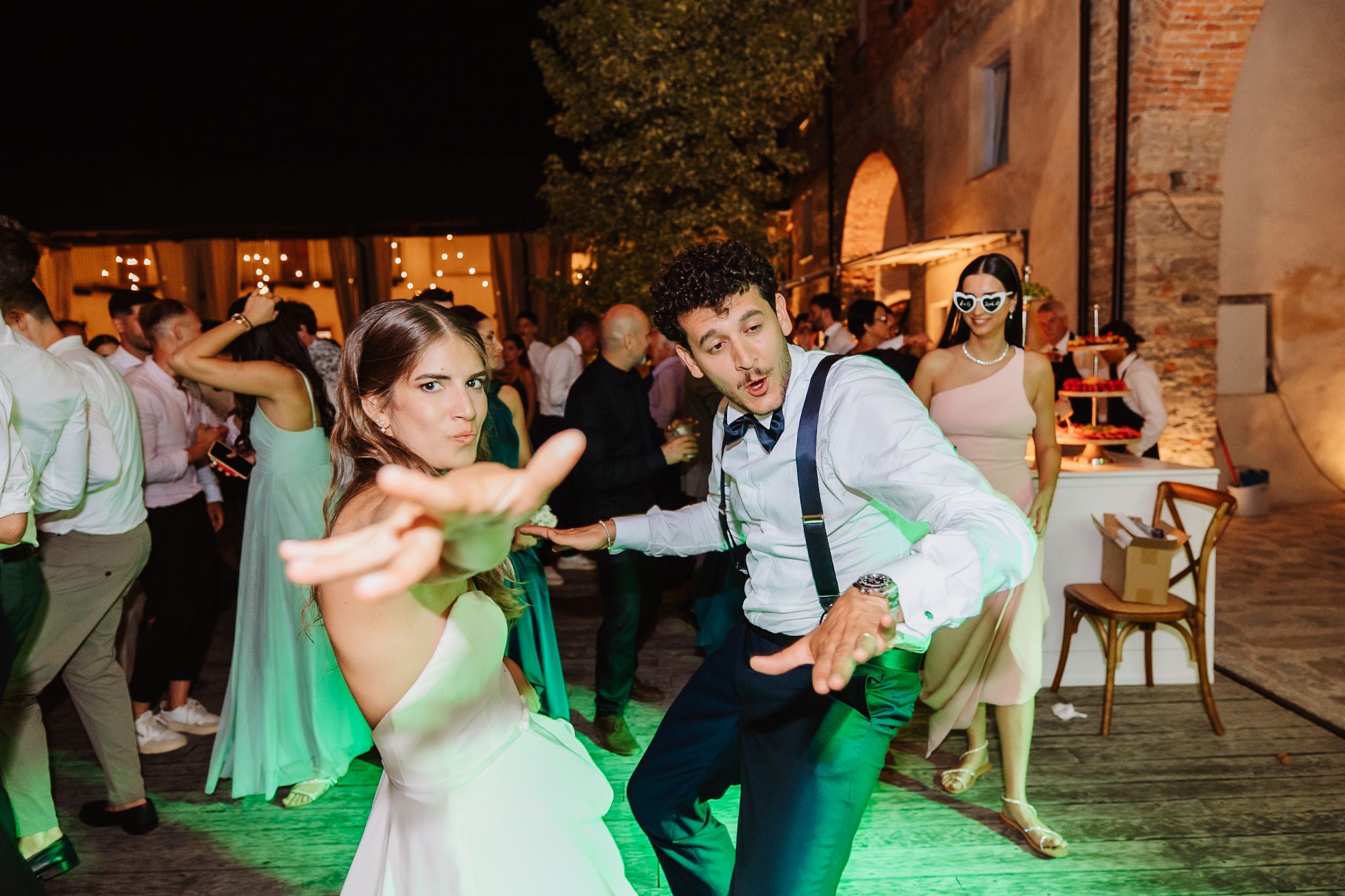 Wedding guests dancing energetically on a dance floor with green lighting at an outdoor evening reception.