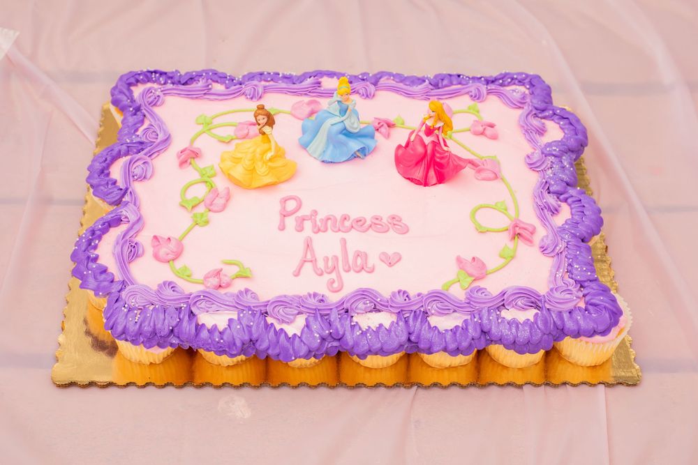 Pink and purple frosted cupcakes arranged into a princess-themed cake with decorative floral details and borders.