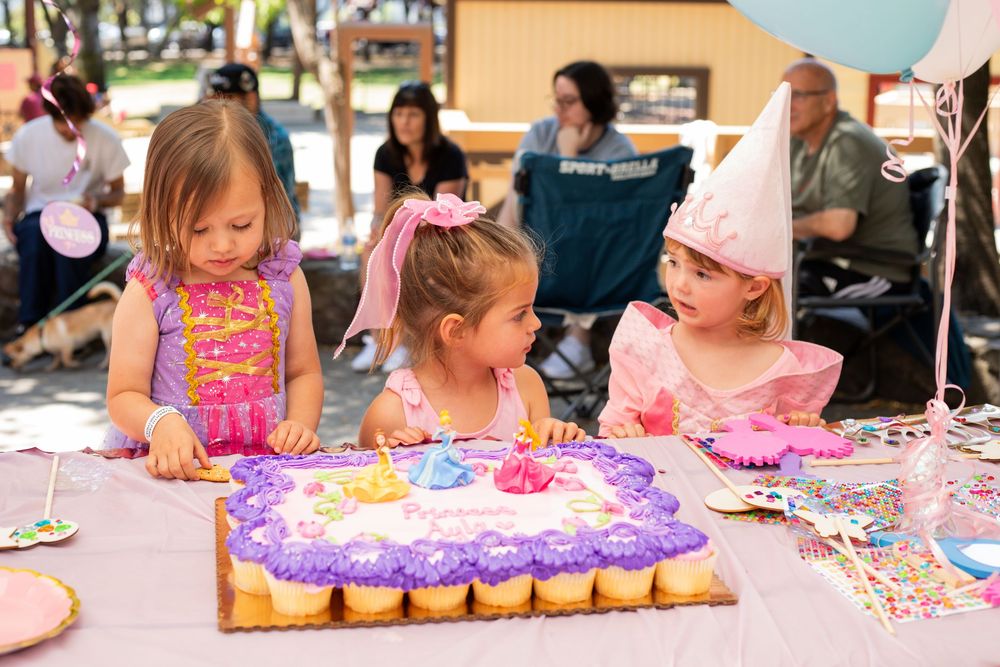 A panoramic view of a birthday party table filled with decorations, cupcakes and kids enjoying party activities.