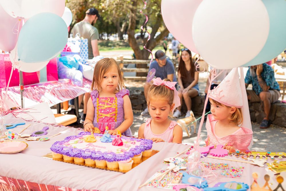 A festive birthday party scene with pink and white balloons, decorations and cupcakes on a decorated table.