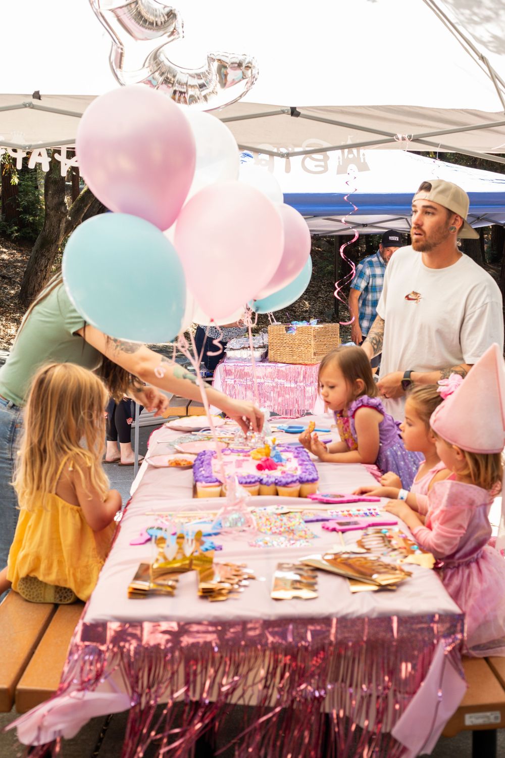 Festive birthday party table decorated with pink and blue balloons and colorful cupcakes at an outdoor celebration.