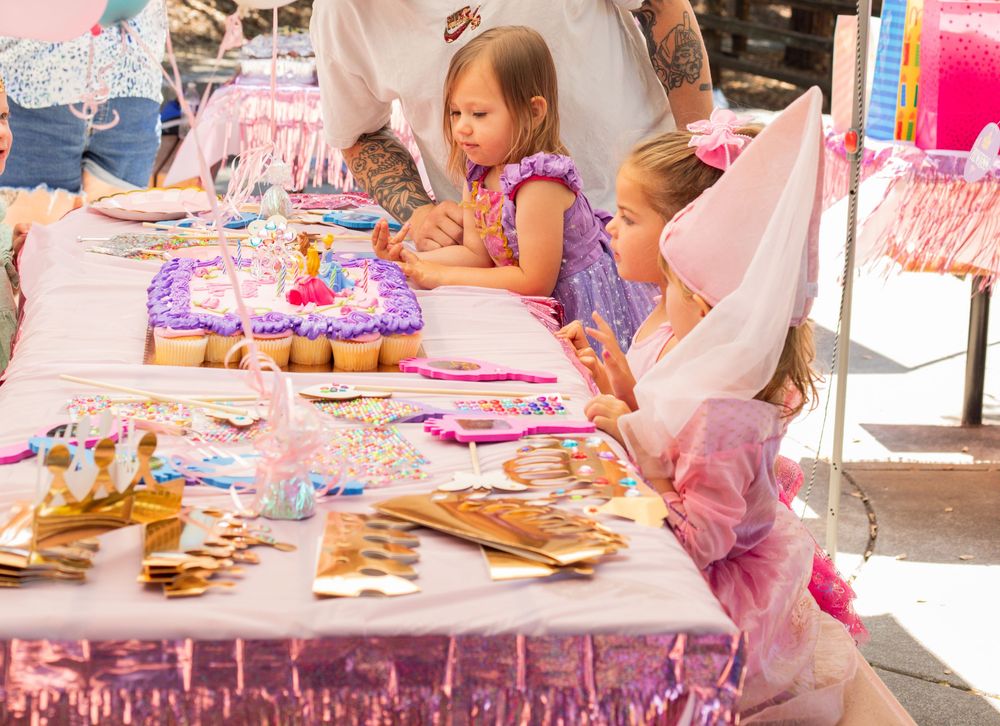 Children enjoy making arts and crafts at a long pink-themed party table decorated with creative supplies.