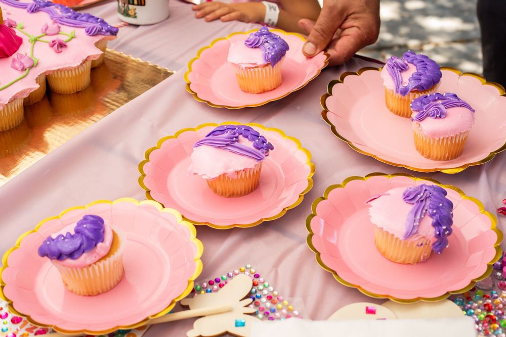 Pink frosted cupcakes with purple decorative bows arranged on scalloped plates at a party dessert table.