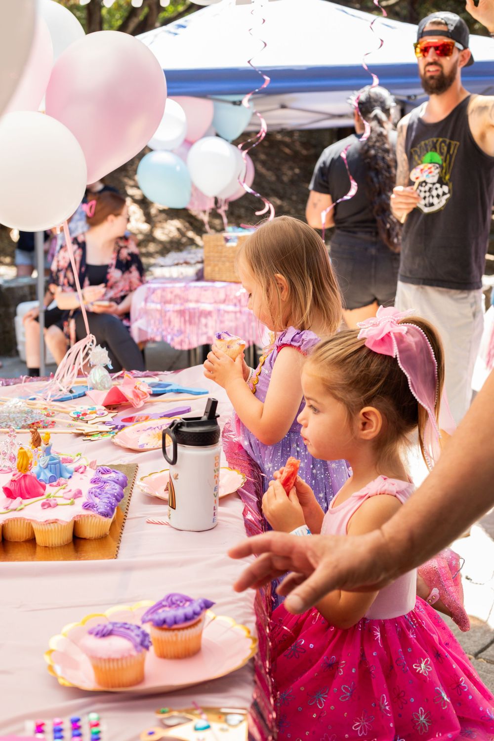 Kids gathered around a table decorated with pink balloons and cupcakes at a birthday party celebration.