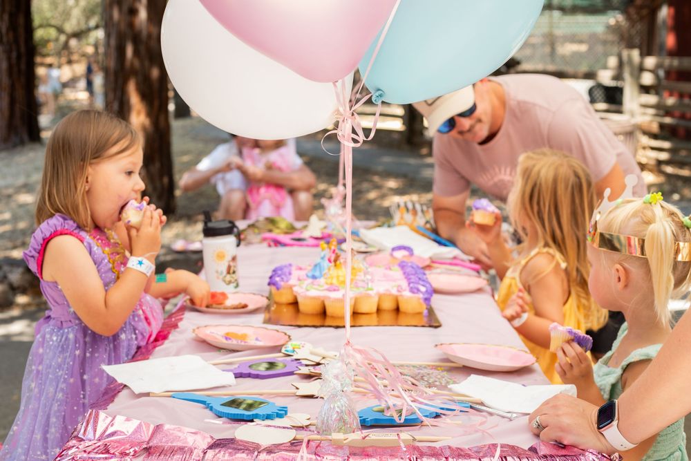 Children decorating cupcakes at a fun party with pink and blue balloons in the background.