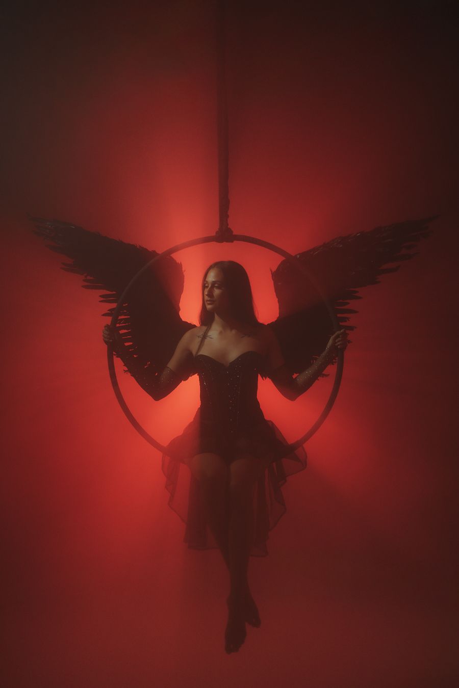 Performer spreads wings midair, glowing red light adds theatrical intensity, South Florida Mannyportraits photography for aerial creatives.