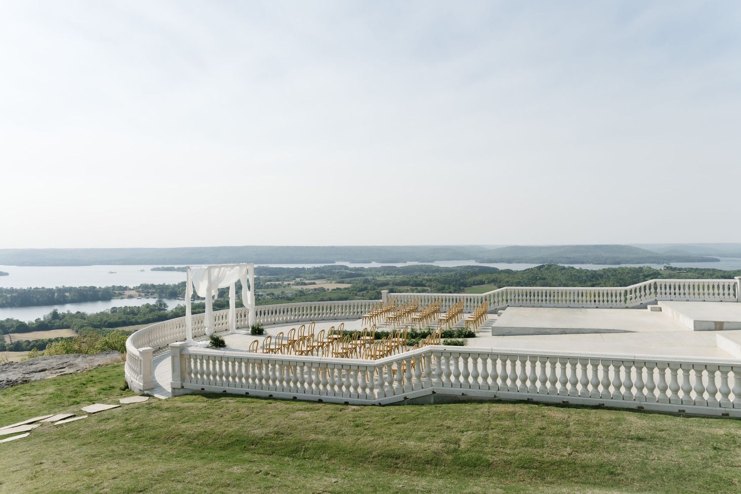 Elegant outdoor wedding venue on a hilltop terrace with white balustrades overlooking a scenic river landscape.