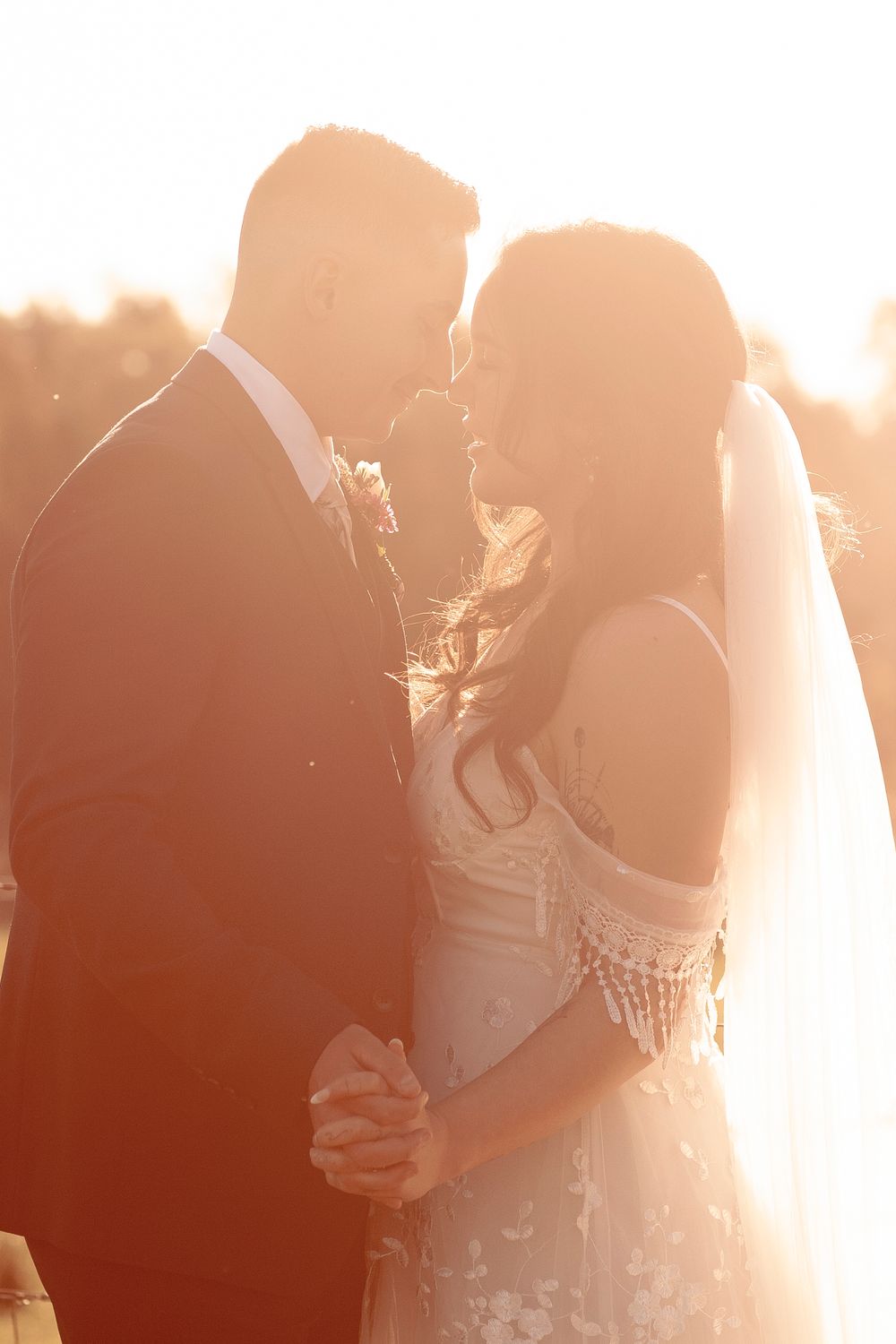 Newlywed couple shares an intimate moment at sunset backlit by golden light, captured in a romantic wedding photo.