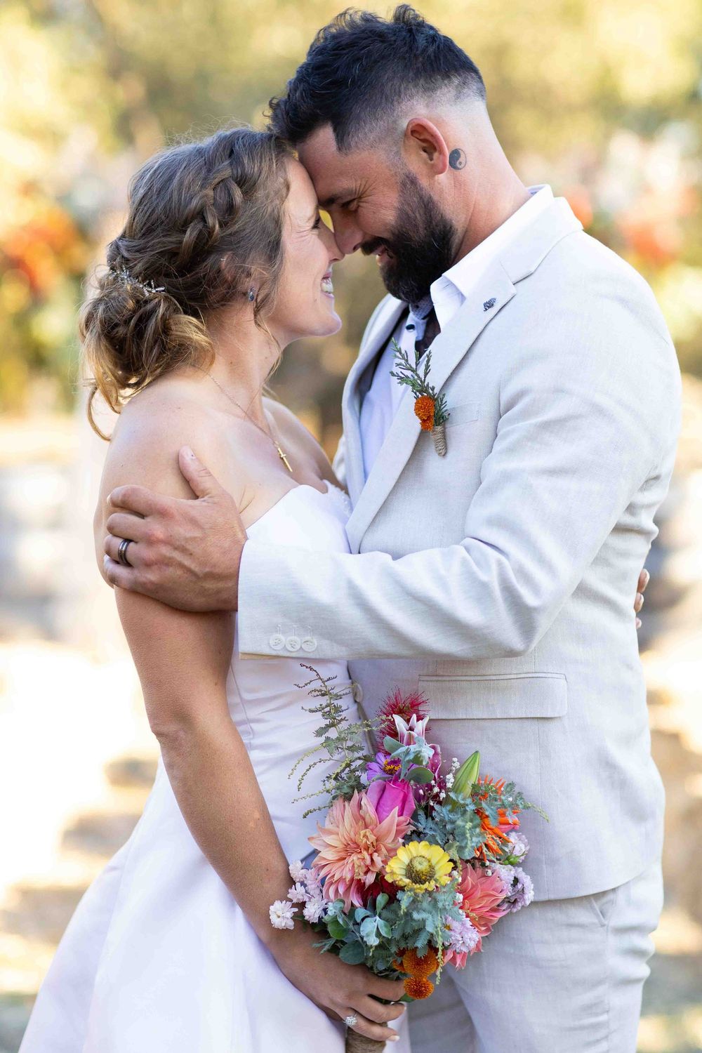 A romantic wedding moment outdoors with white attire and a vibrant bouquet of pink, orange and yellow flowers.
