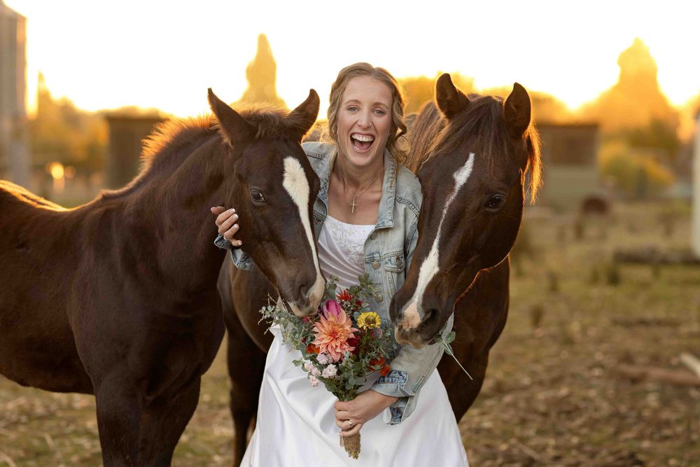 A joyful moment with two brown horses and a bouquet of flowers during a sunset photo shoot in a field.