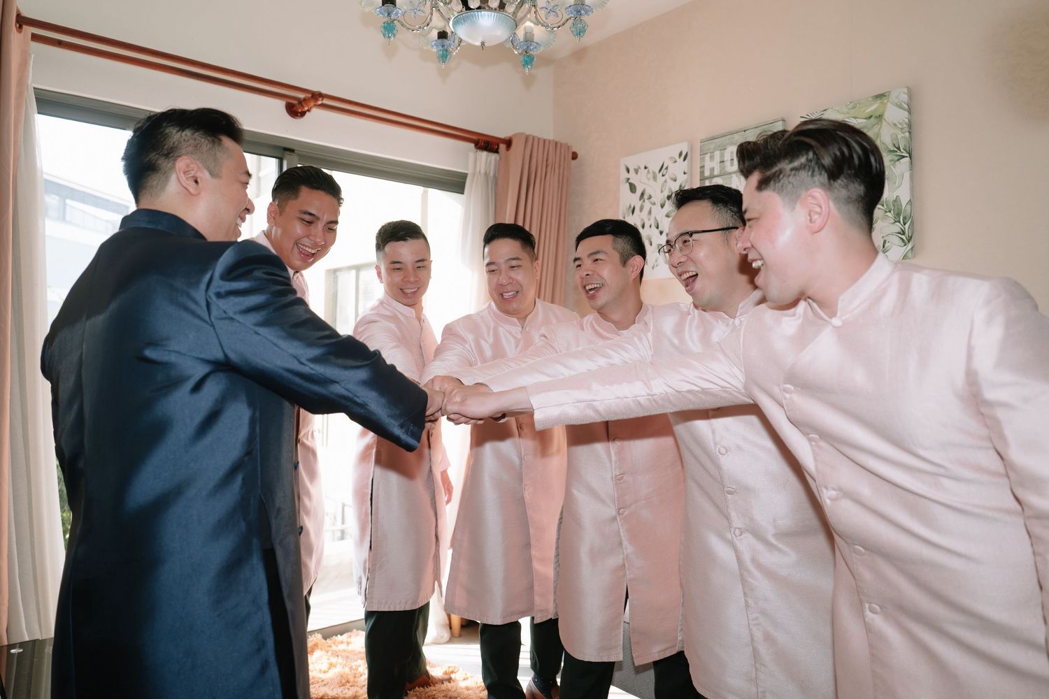 Groom in blue suit doing a group handshake with groomsmen in pink barong shirts.