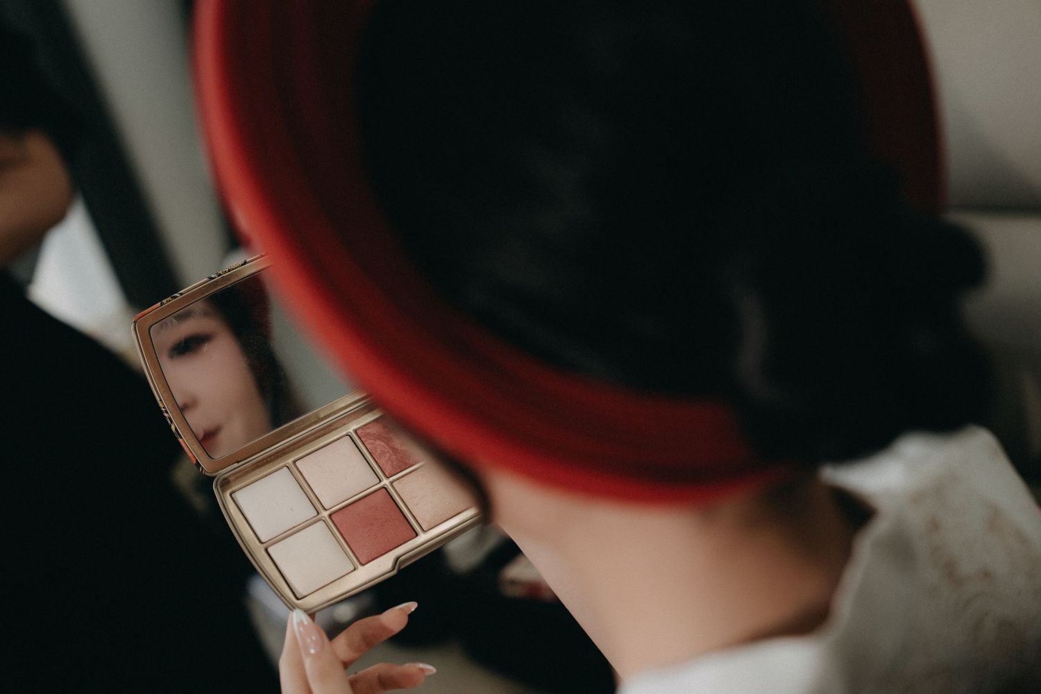 Bride viewing makeup palette in compact mirror during wedding preparation.