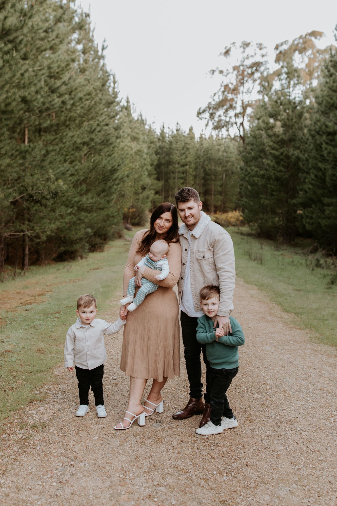 Parents and their little boys cuddle in a open Adelaide green forest at golden hour during a family photography session with Lauren Lunn.