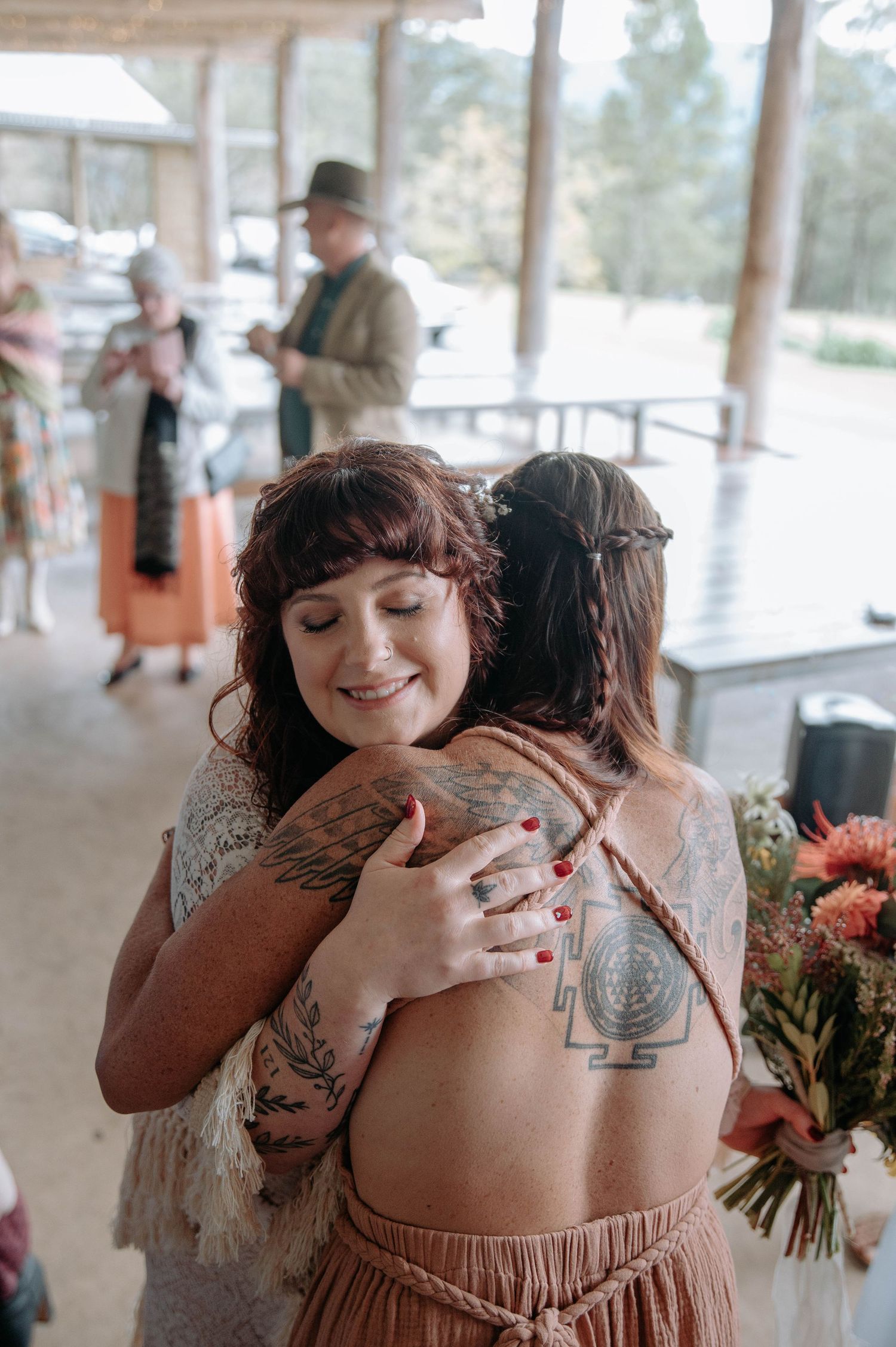 Two people share an emotional embrace during what appears to be a wedding celebration with flowers nearby.