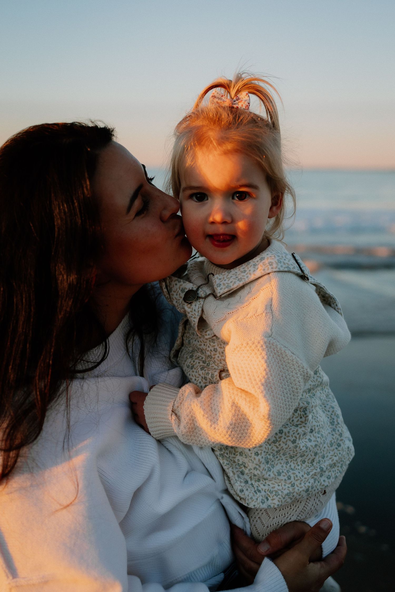 A tender moment captured at sunset by the ocean as warm golden light illuminates their faces.