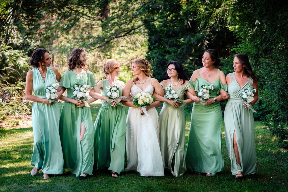 Bridesmaids in mint green dresses seated together on outdoor steps.