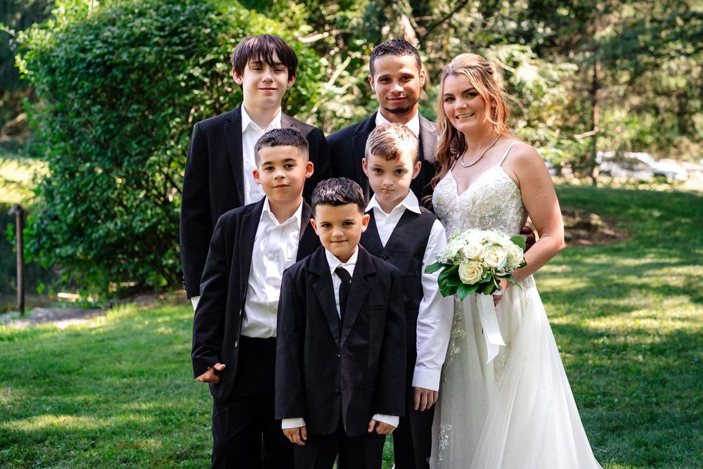 Wedding ceremony participants pose for photos in a garden setting with greenery and natural light.
