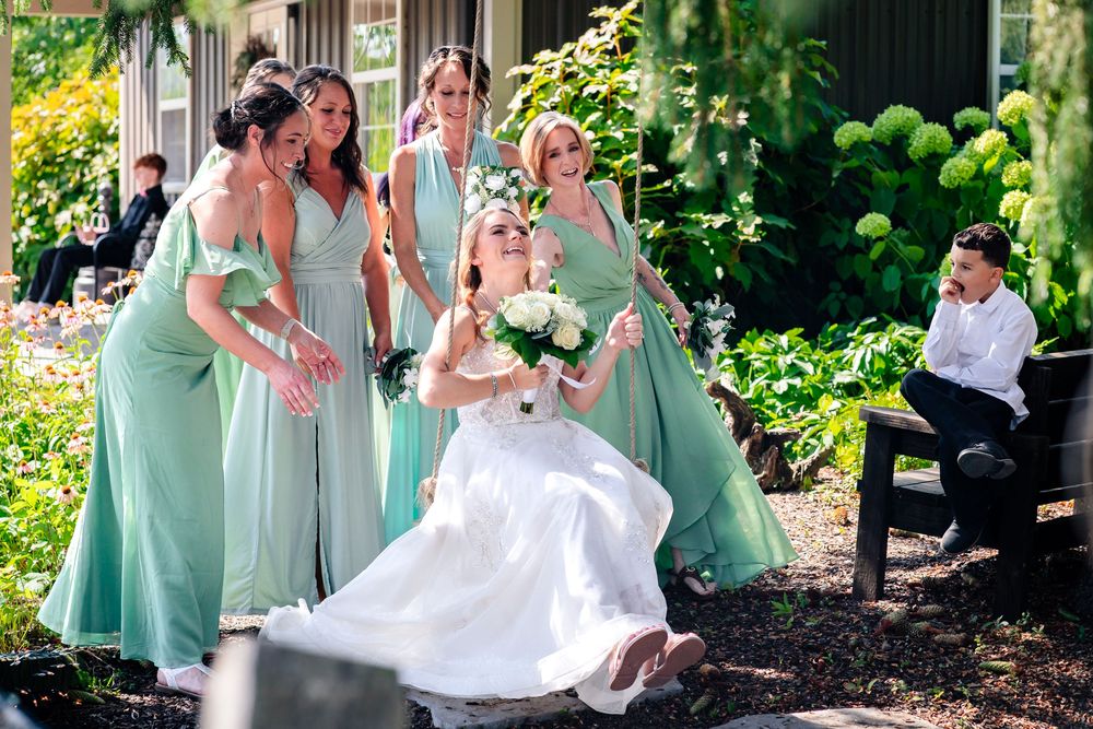 Wedding party members in sage green dresses and black suits gather for outdoor photos.