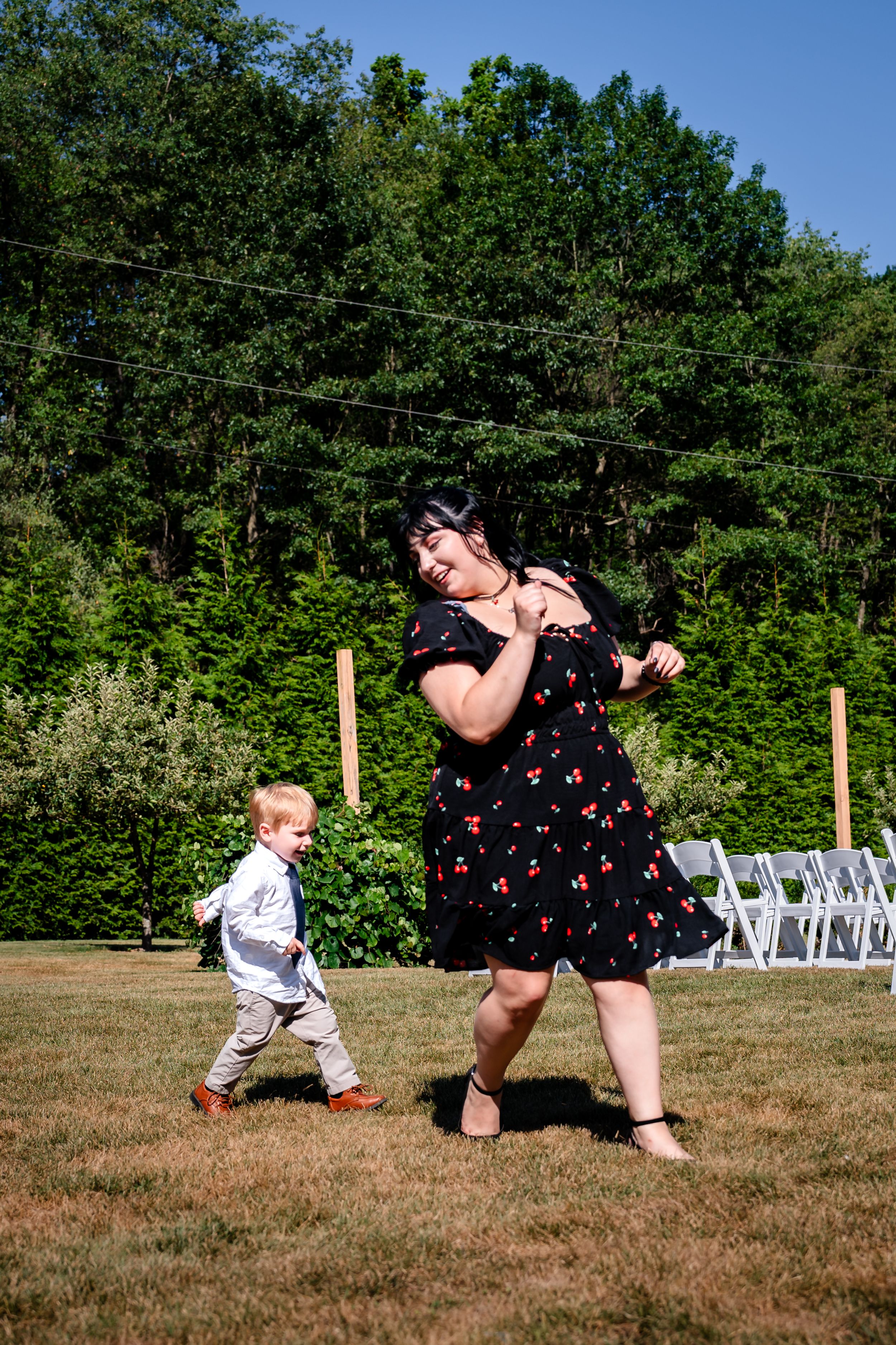 Playful sequence of a guest chasing a small child across a grassy outdoor wedding venue.