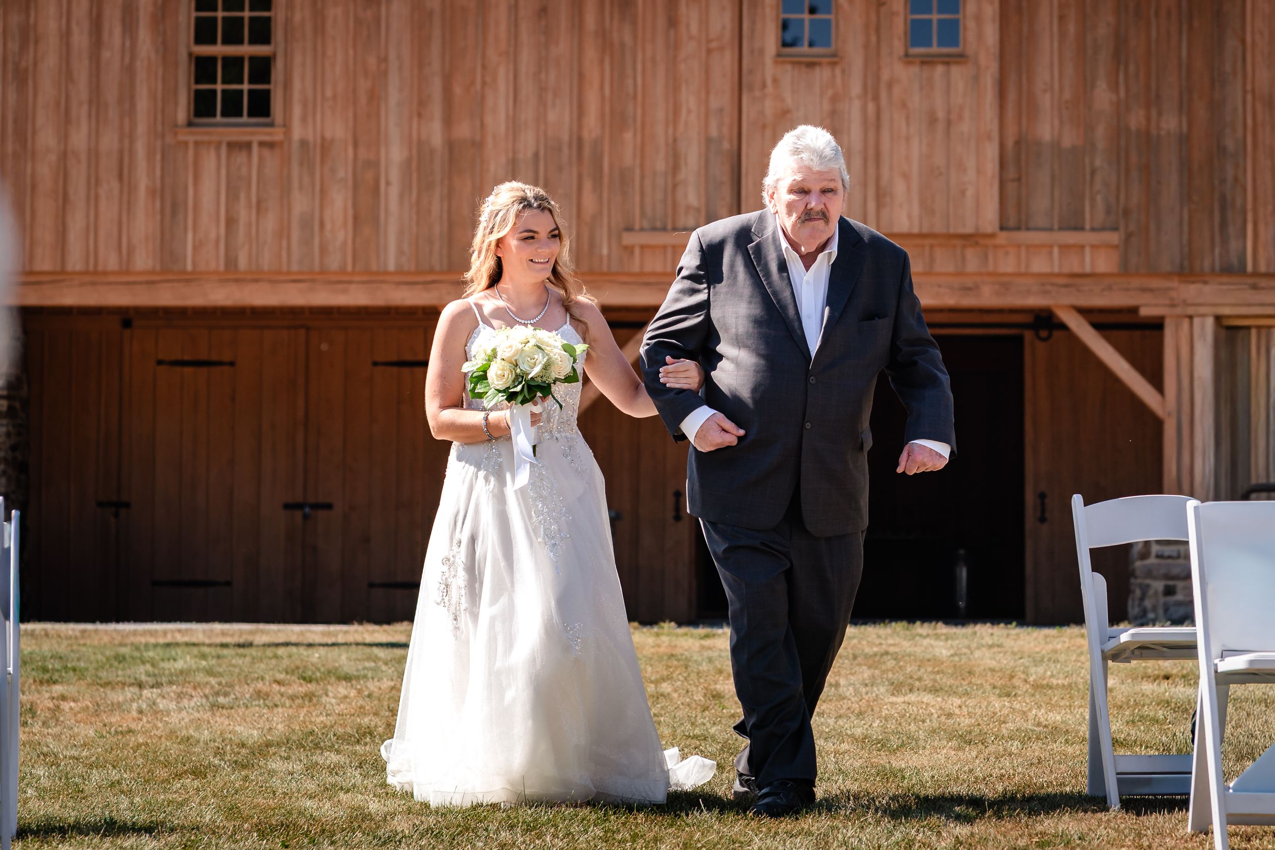 Rustic wooden barn exterior serves as backdrop for an outdoor wedding ceremony.