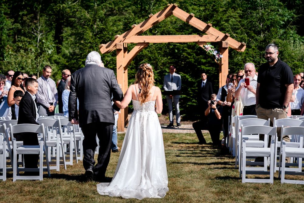 Outdoor wedding ceremony setup with white chairs and wooden arch against natural landscape.