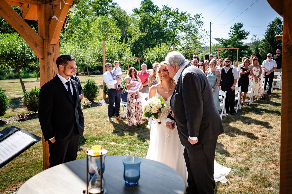Wedding ceremony procession taking place at an outdoor venue with wooden pergola.