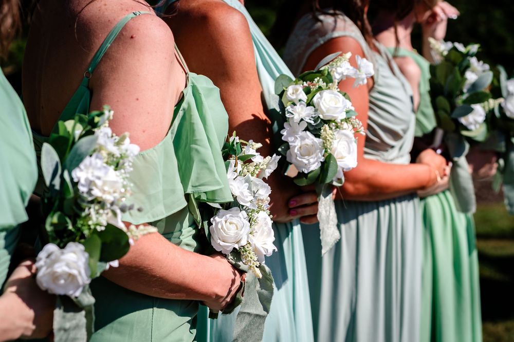 Bridesmaids in mint green dresses hold white floral bouquets during outdoor wedding.