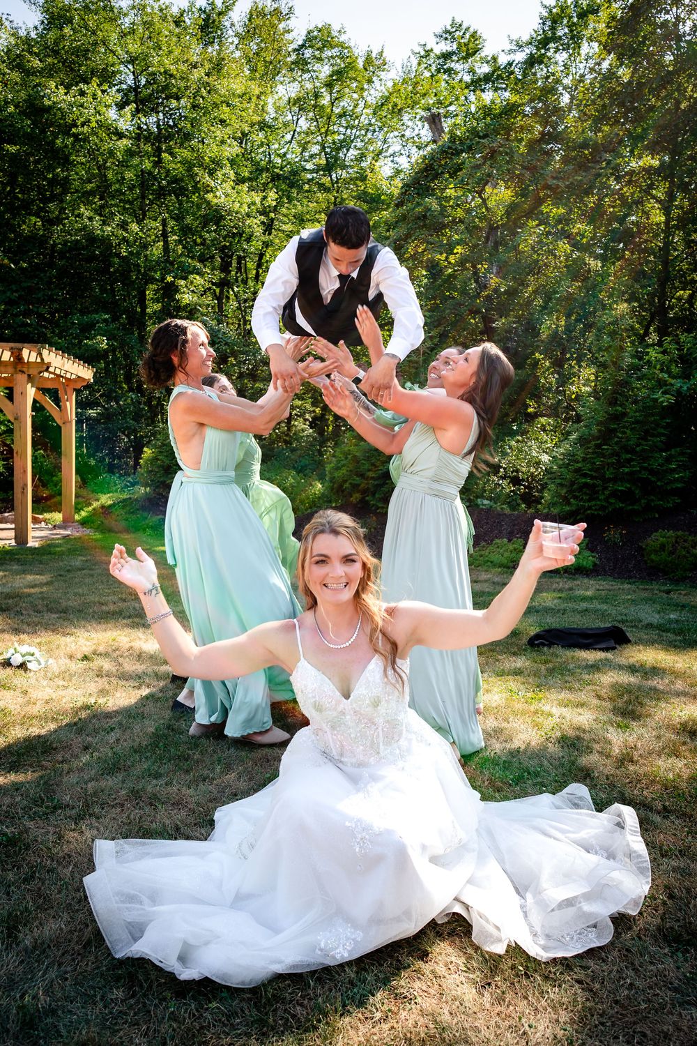 Wedding party in mint green dresses poses playfully on grass.