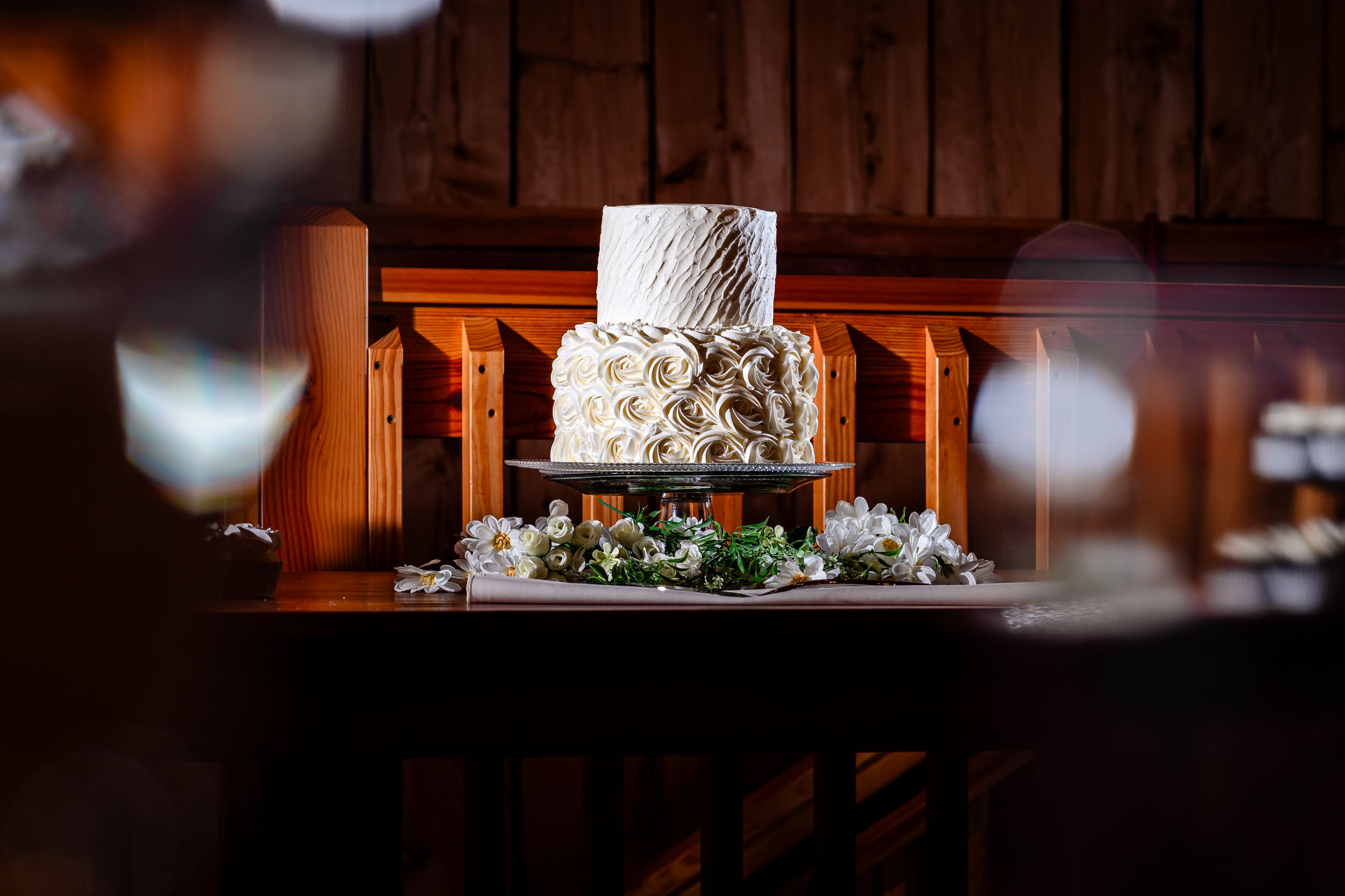 Wedding cake and floral decorations displayed in warm rustic barn lighting.