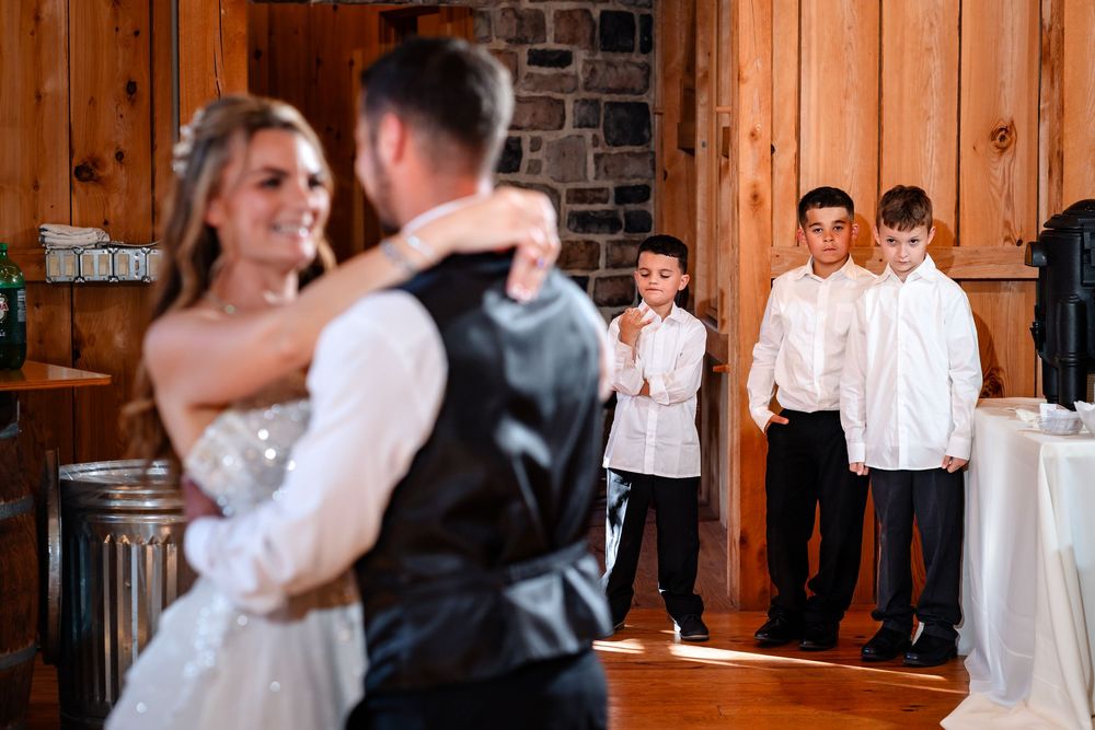 Wedding reception dance in a rustic wooden barn with string lights overhead.