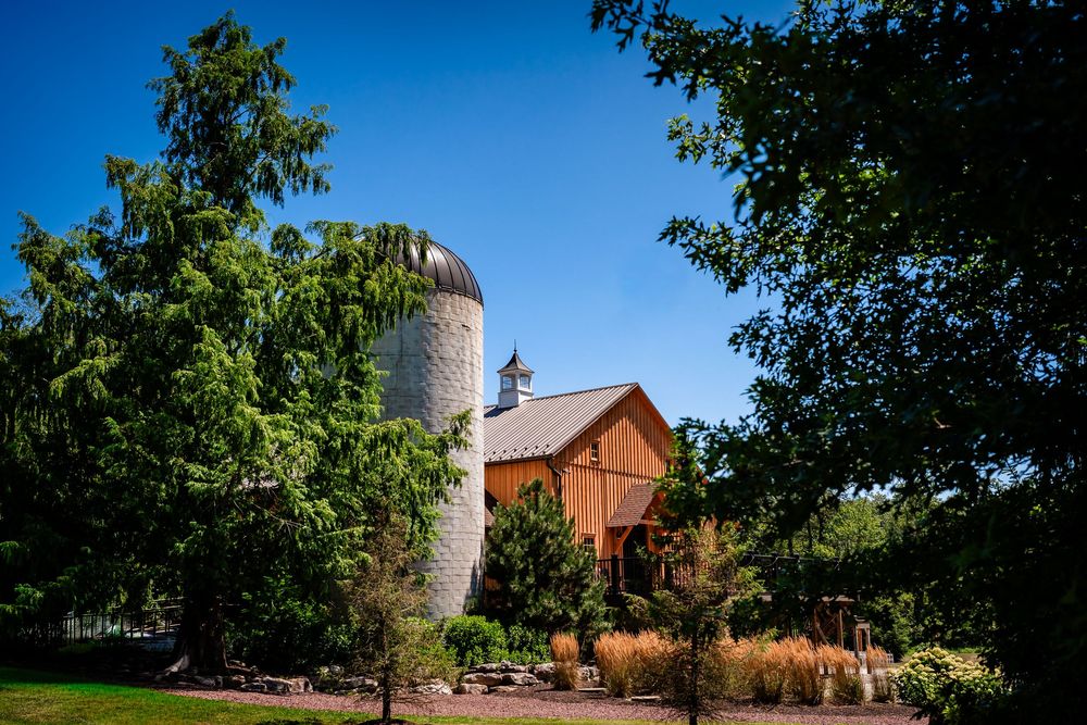 Panoramic view of a rustic barn venue surrounded by trees under blue summer sky.