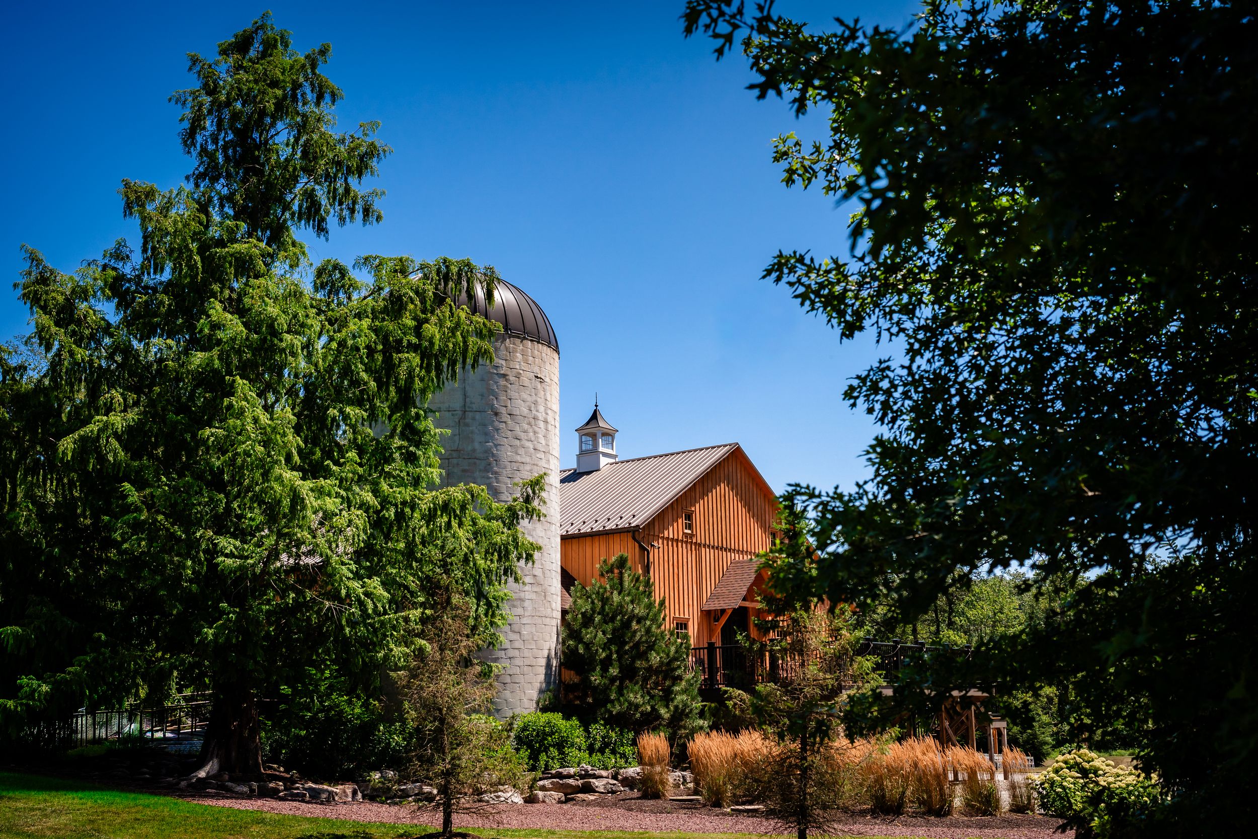 Panoramic view of a rustic barn venue surrounded by trees under blue summer sky.