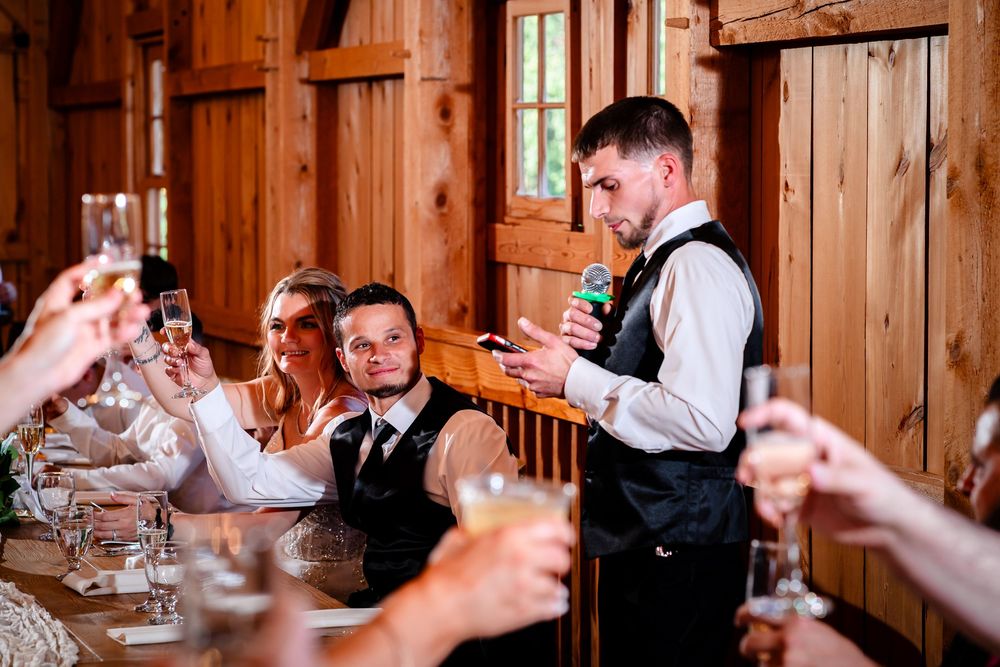 Wedding guests raise their glasses for a celebratory toast in a rustic wooden barn venue with string lights.