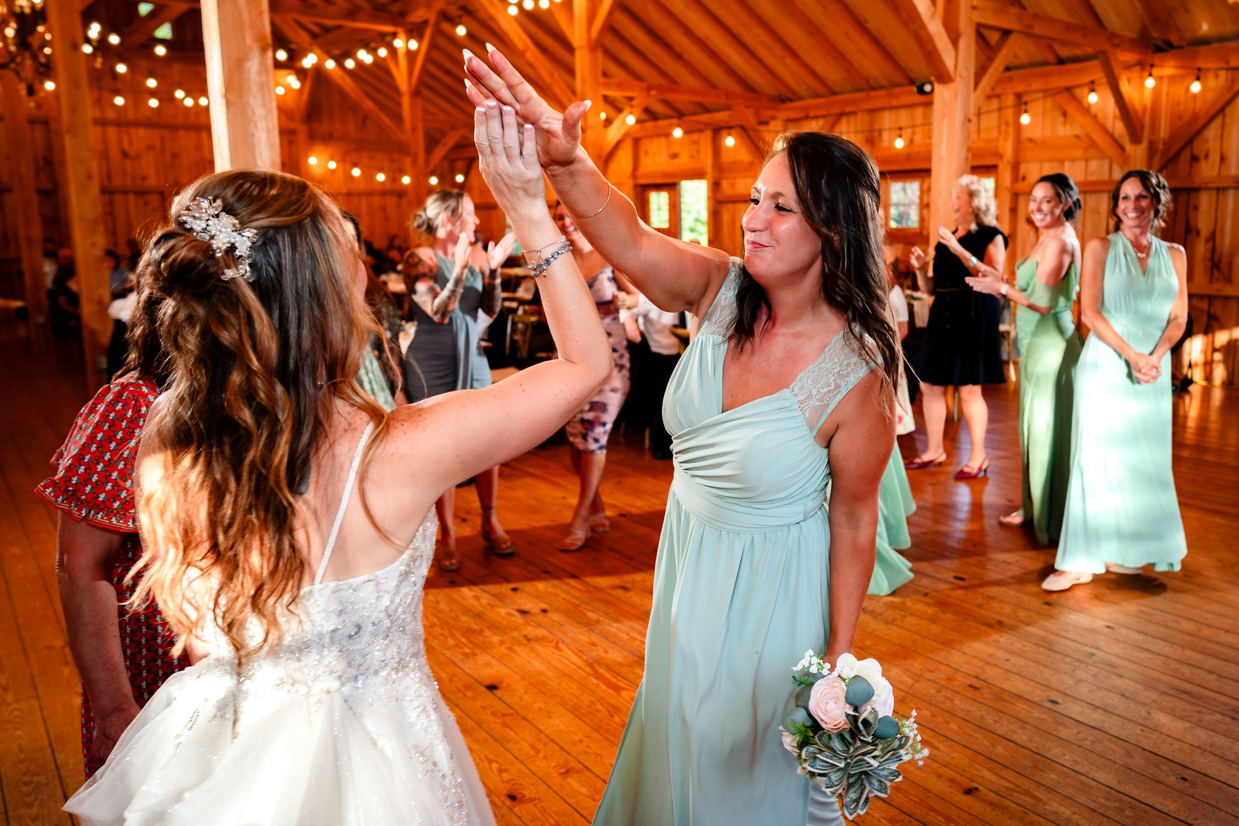 Wedding party members in mint green dresses celebrate during reception in wooden barn venue.