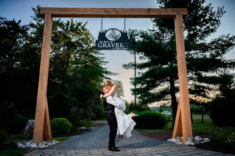 Wedding couple poses under wooden archway at sunset.
