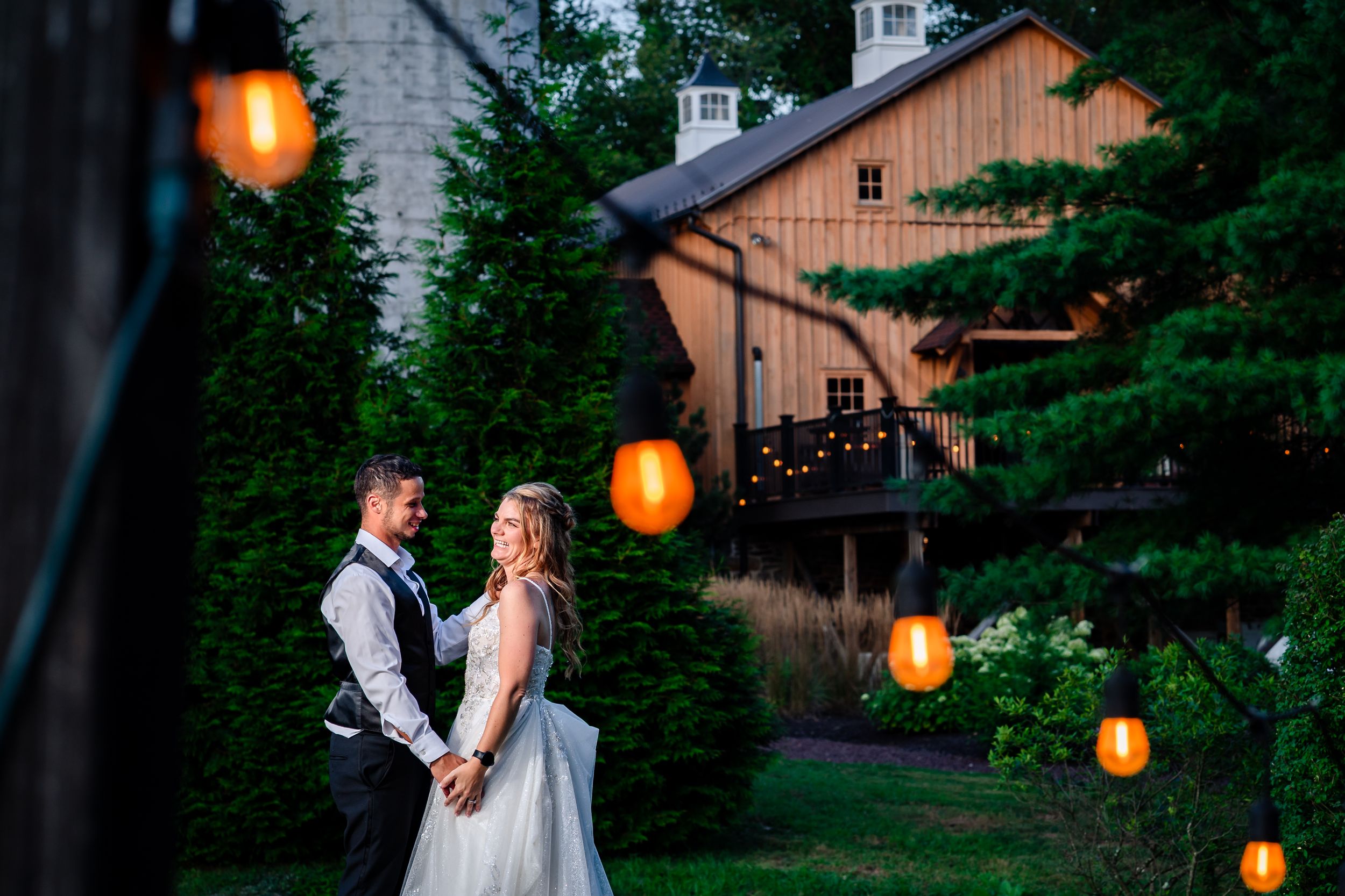 Evening wedding photos with glowing string lights and rustic barn backdrop.